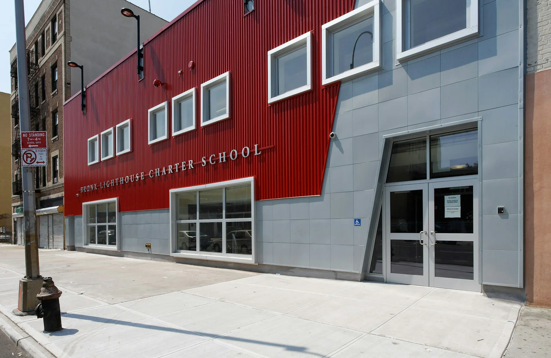 Contemporary charter school facade featuring red corrugated metal panels and gray composite cladding with horizontal window bands and glass entry doors by Gran Kriegel Associates Architects and Planners.