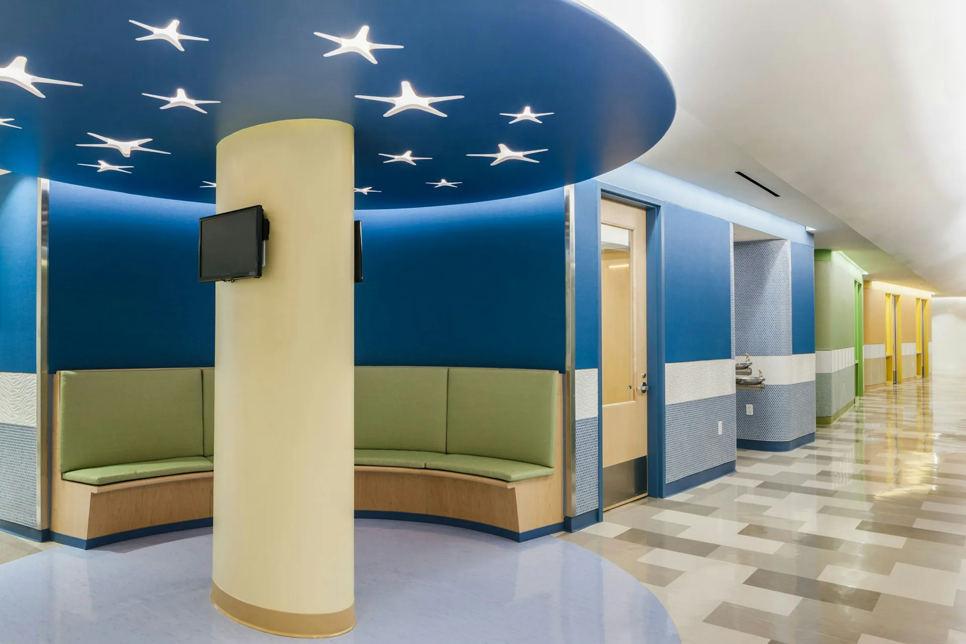 Modern corridor with curved seating booth featuring blue starry ceiling, cream cylindrical column, green upholstered seating, and polished floor by Gran Kriegel Associates Architects and Planners.