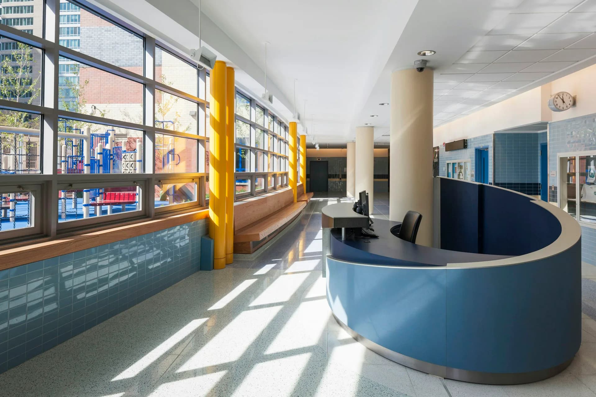Modern library or educational interior with curved blue desk, yellow structural columns, large windows, and custom millwork displaying materials, designed by Gran Kriegel Associates Architects and Planners.