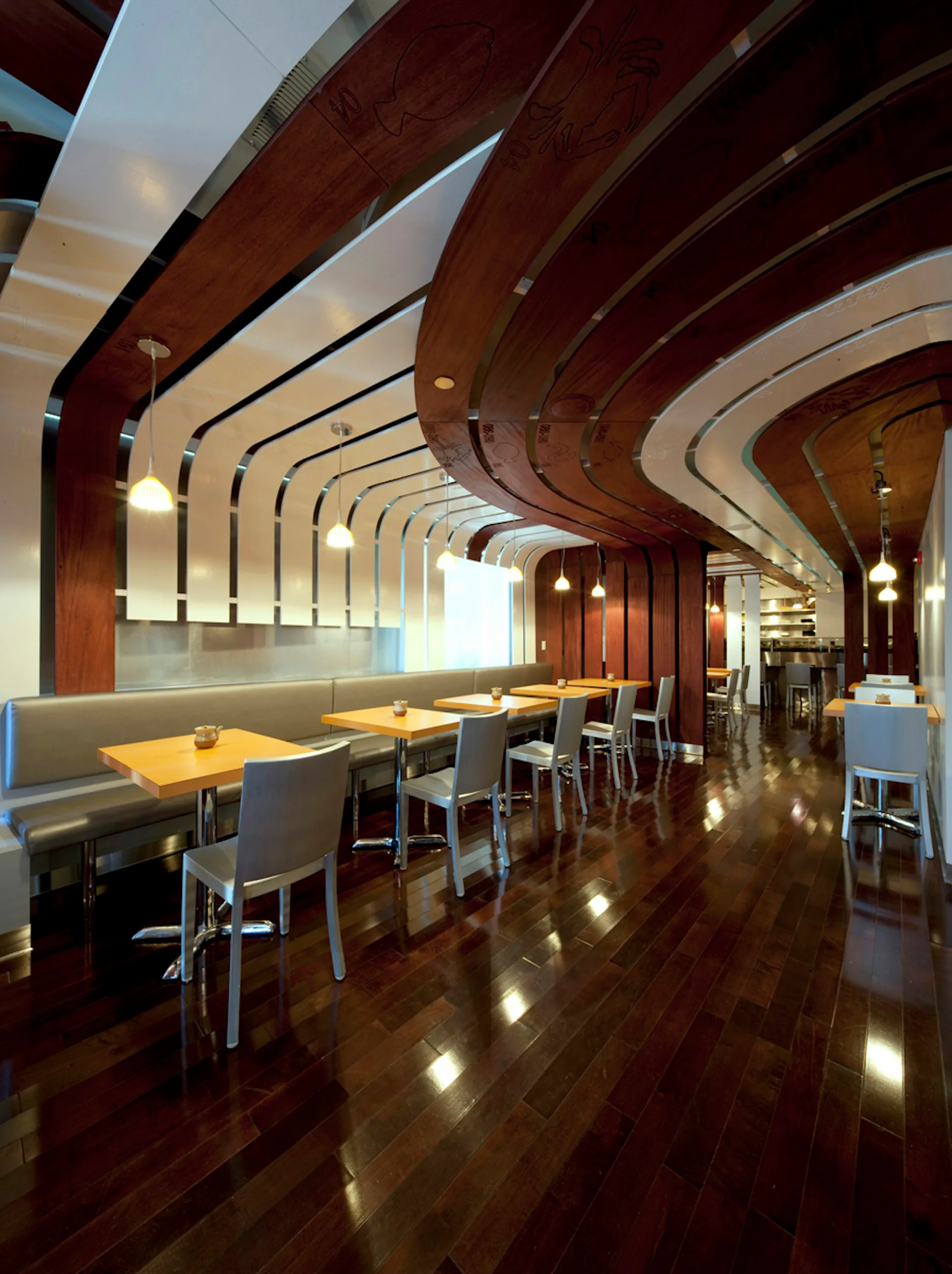 Modern restaurant interior with curved wooden beam ceiling, continuous banquette seating, yellow tables, and polished dark wood flooring by GRO Architects.