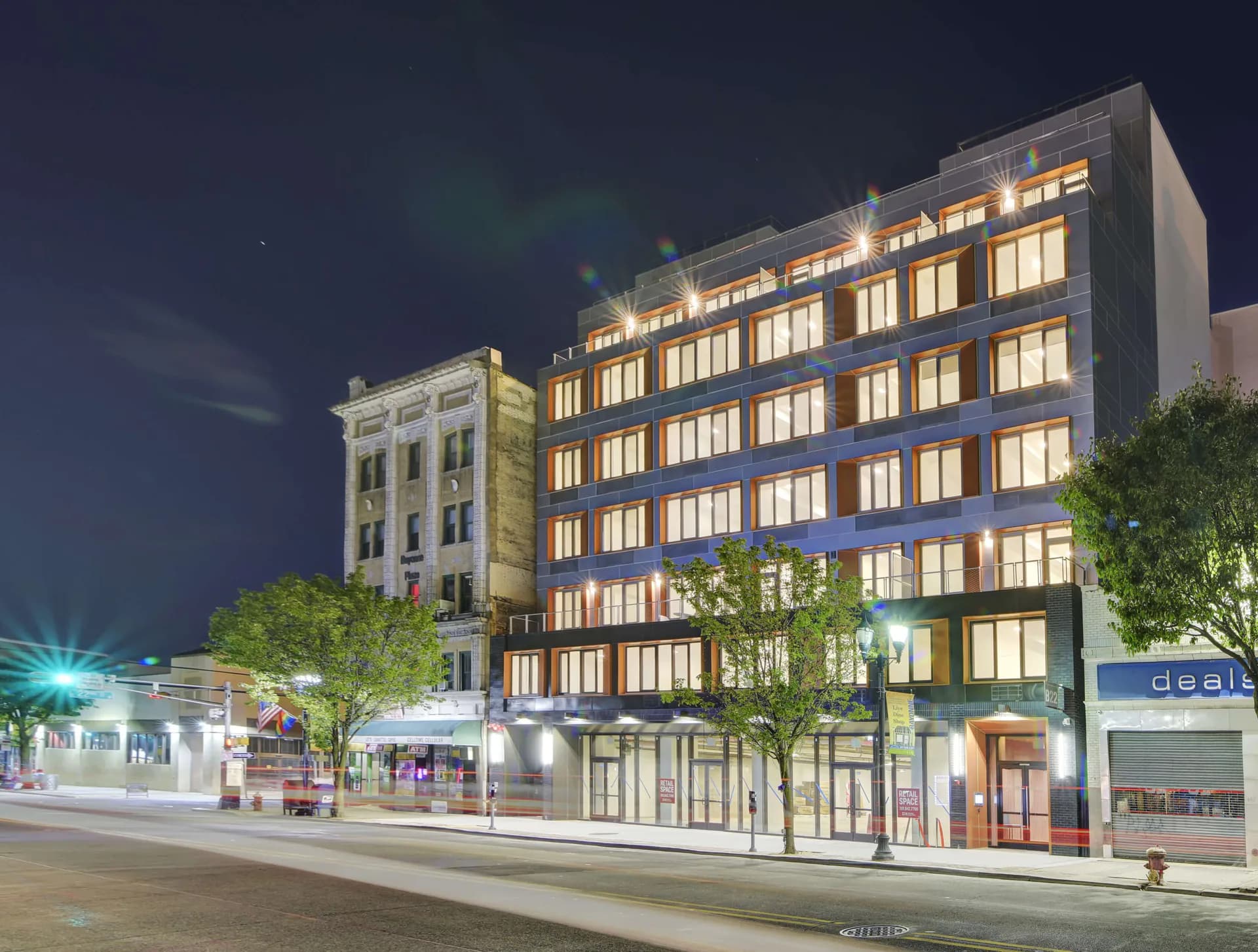 Nighttime architectural rendering of an illuminated mixed-use building facade with symmetrical windows and ground-floor retail, featuring synthetic lighting and idealized material presentation by GRO Architects.
