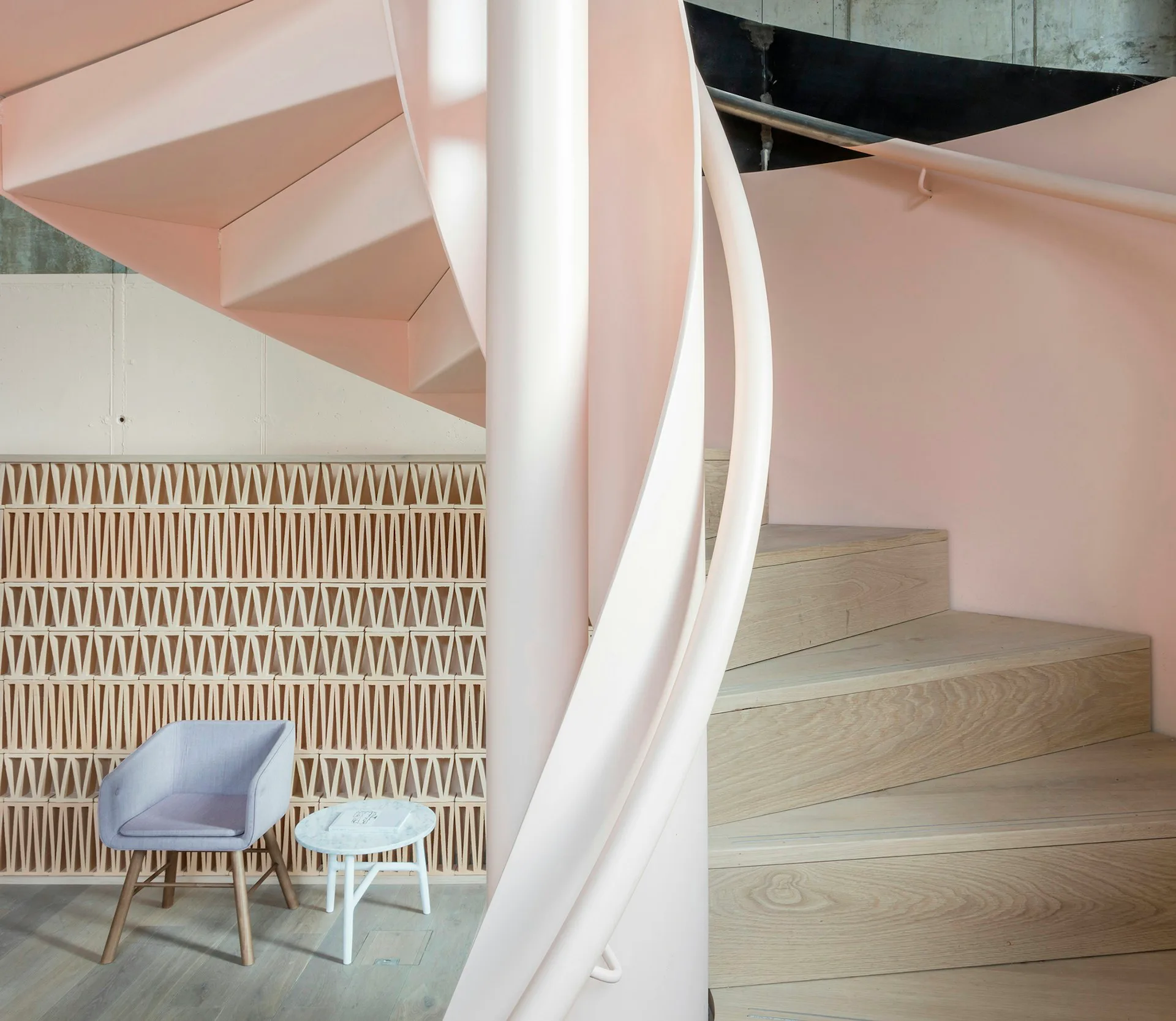 Modern interior with curved white structural elements, pale pink walls, geometric patterned feature wall, wooden stairs, and mid-century blue chair by Grzywinski+Pons.