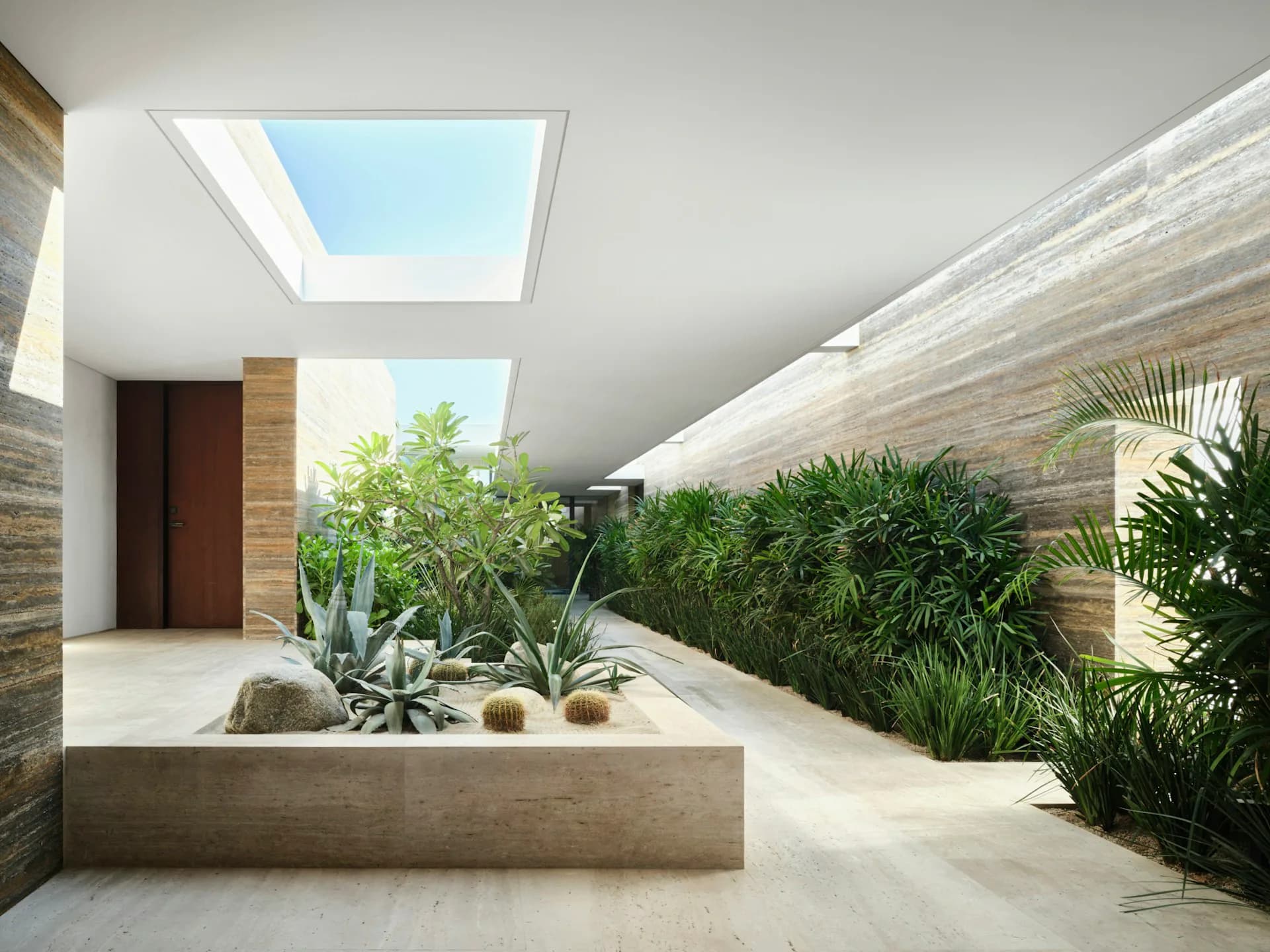 Modern interior courtyard with skylight, concrete planter beds, lush vegetation, and natural stone walls by Guerin Glass Architects.