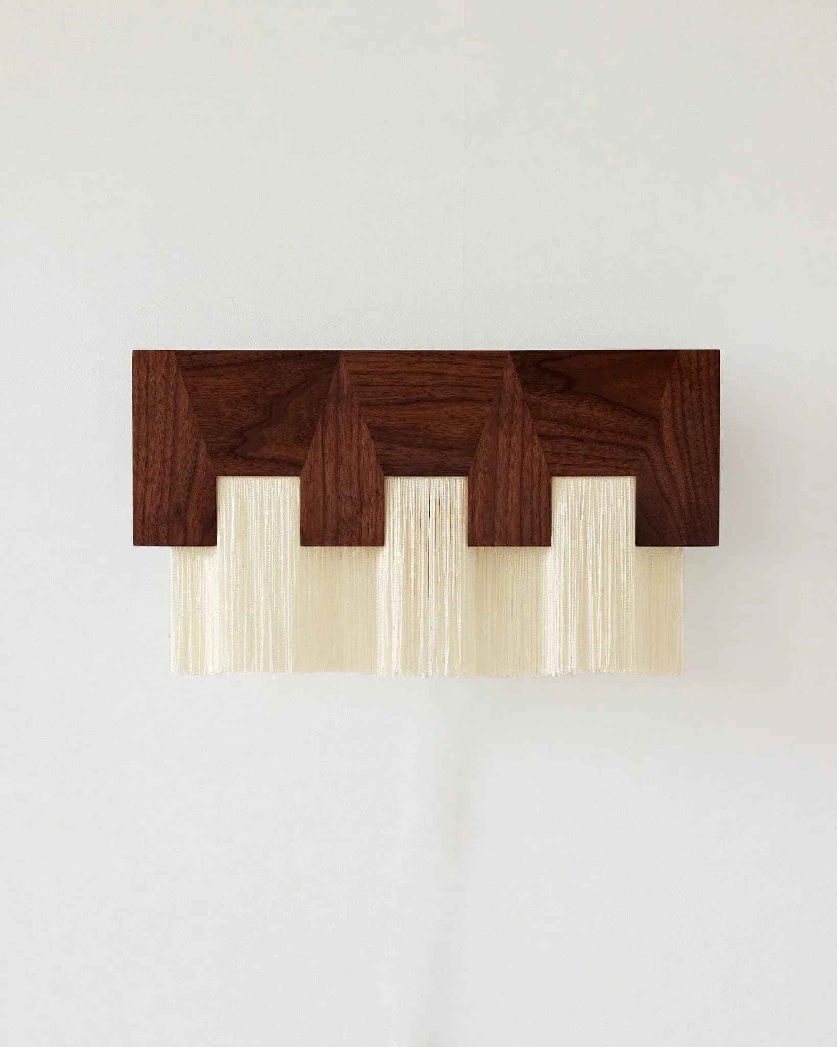 Dark wood valance with three rectangular openings and cream pleated fabric panels beneath, mounted on white wall by H. Bigeleisen Studio.