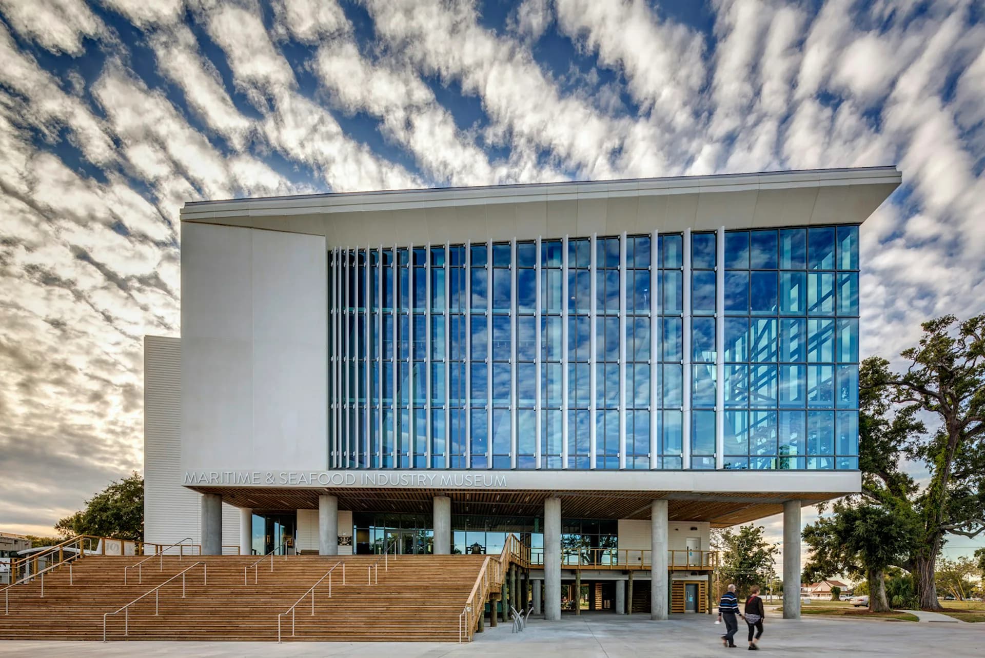 Modern institutional building with white facade, vertical blue-tinted glass panels, and wooden plaza with stairs, designed by H3 Hardy Collaboration Architecture, LLC.