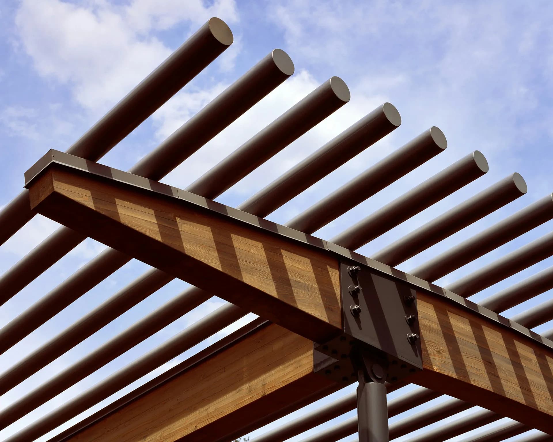 Wooden pergola structure with parallel cylindrical beams extending overhead against a blue sky, showcasing modern architectural design by H3 Hardy Collaboration Architecture, LLC.