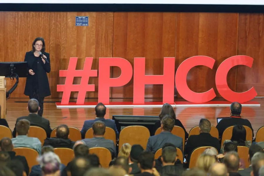 Large red #PHCC letters installed in an auditorium with wooden paneling and a speaker at a podium by Handel Architects.