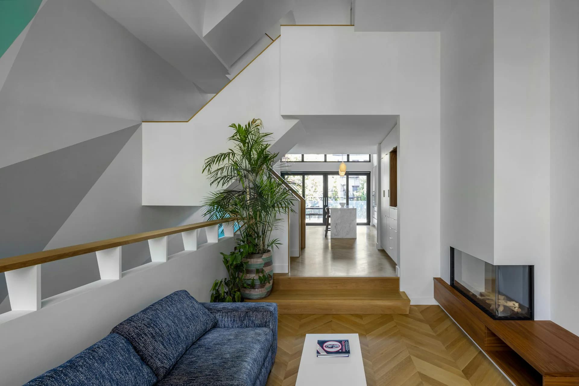 Modern loft interior with white walls, wooden herringbone flooring, and geometric grey concrete elements; blue upholstered seating and potted plant visible by Hanson Architecture.