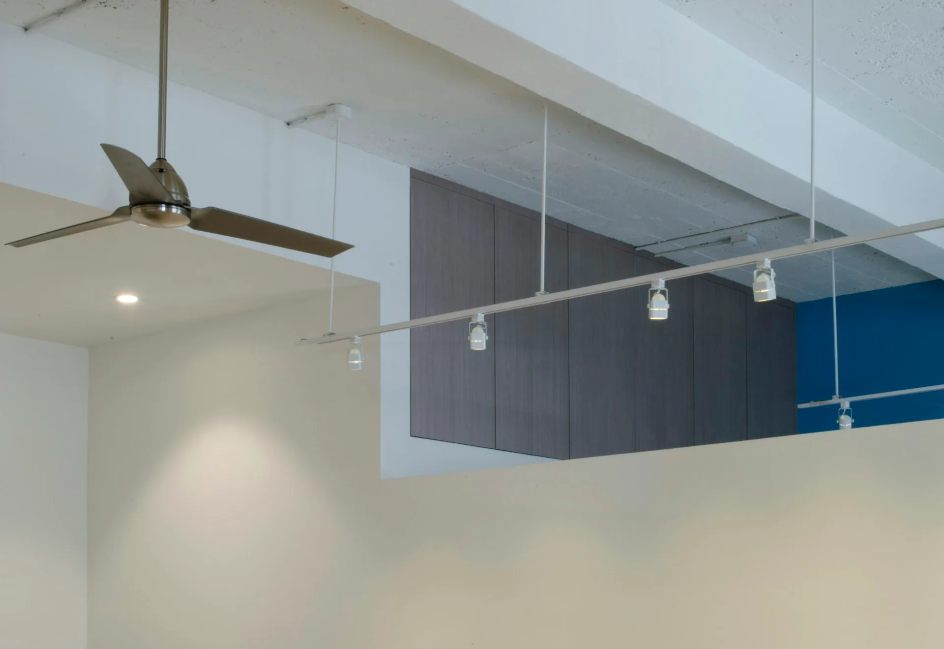 Modern interior space with exposed ceiling, bronze ceiling fan, pendant lights, and blue architectural wall feature by Hanson Architecture.