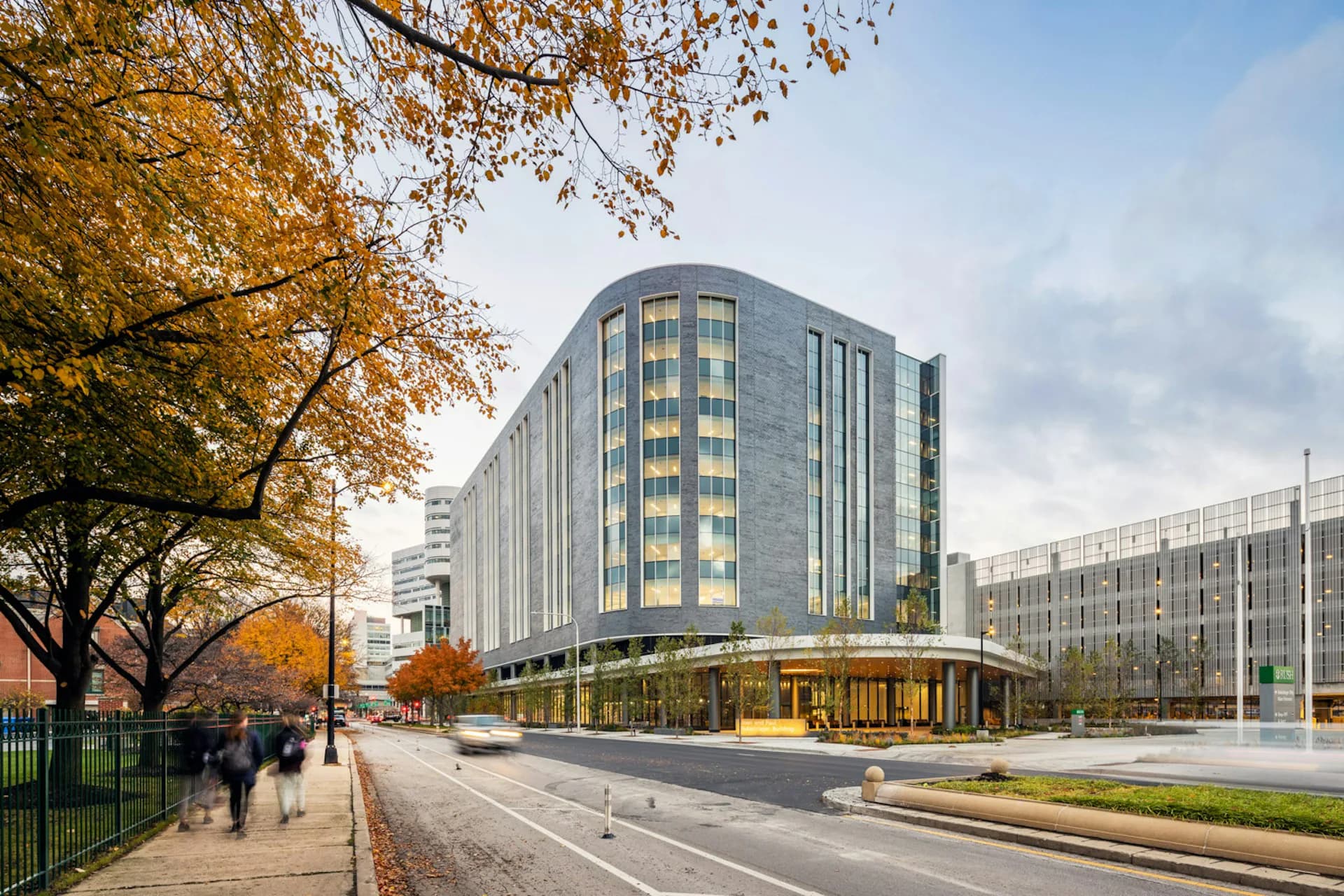 Modern curved residential building with glazed facade and ground-floor retail, autumn streetscape with trees and pedestrians by HDR.