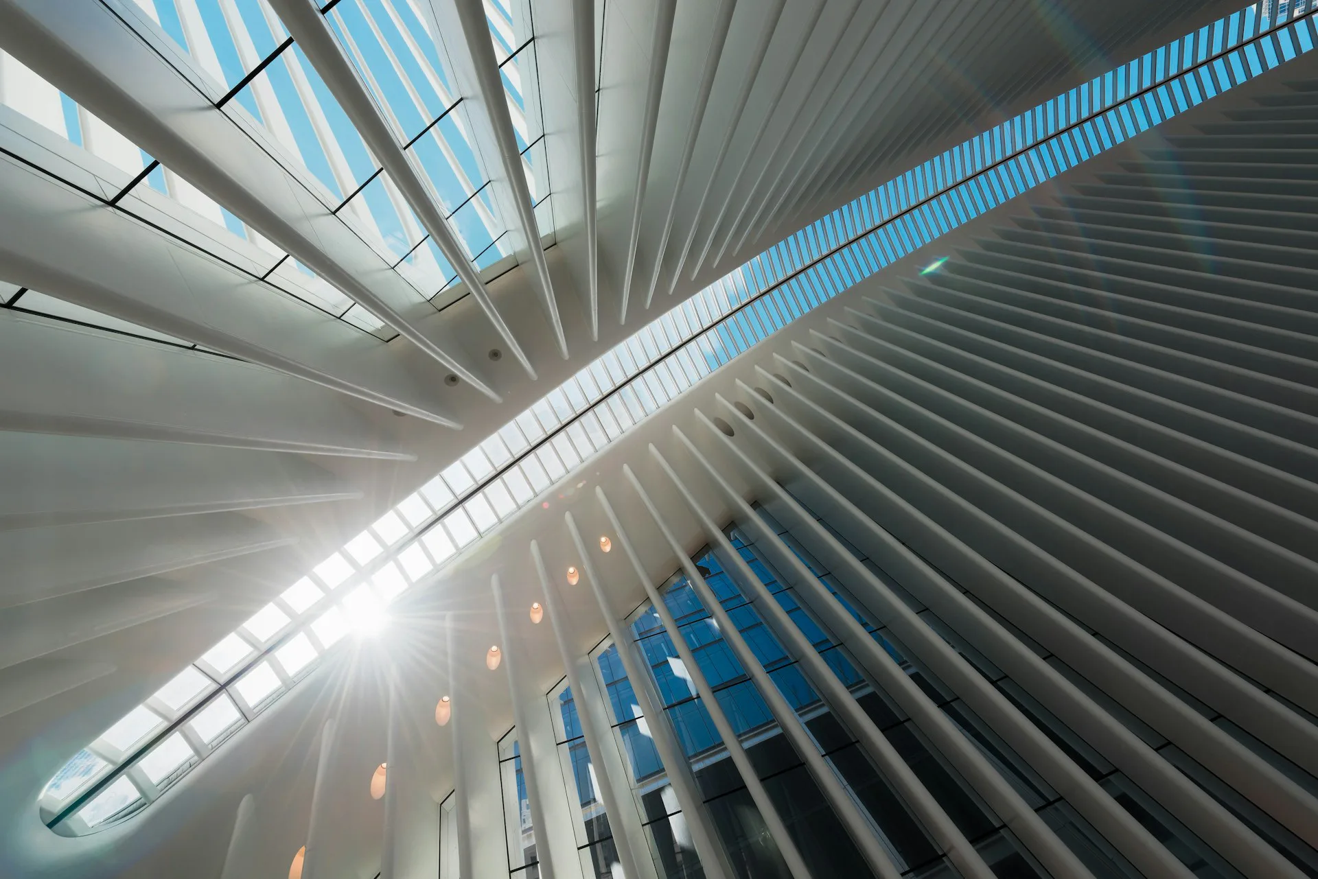 Modern interior atrium with dramatic angular white ribbed ceiling, blue glass panels, and natural skylight flooding the contemporary architectural space by Heintges Consulting Architects & Engineers P.C.