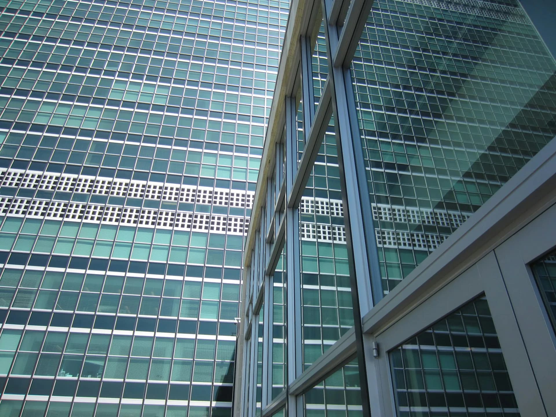 Upward view of modern glass and steel high-rise building facade with geometric window patterns and horizontal white accent bands by Heintges Consulting Architects & Engineers P.C.
