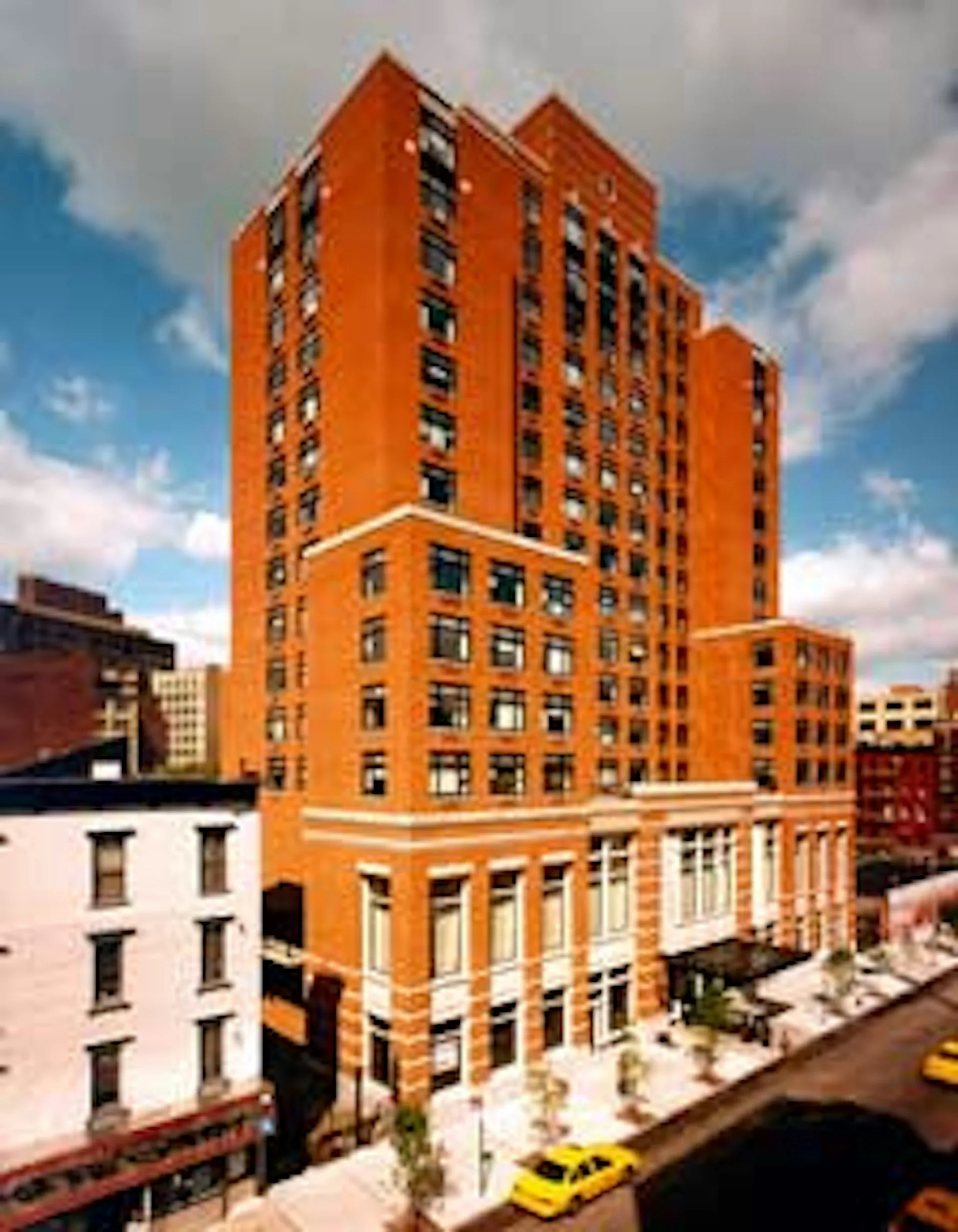 Bright orange brick residential tower with white stone base and horizontal bands, photographed against blue sky with surrounding urban context, by Helpern Architects.
