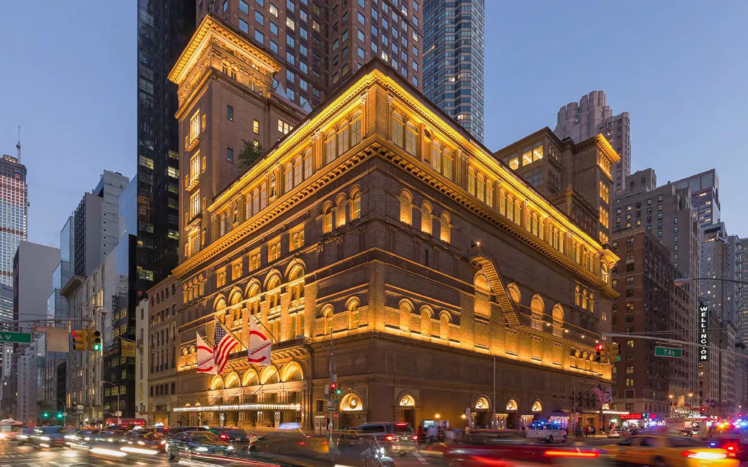 Exterior photograph of Carnegie Hall's historic façade illuminated at dusk, showcasing ornate Romanesque Revival architecture with arched windows and detailed stonework by Helpern Architects.