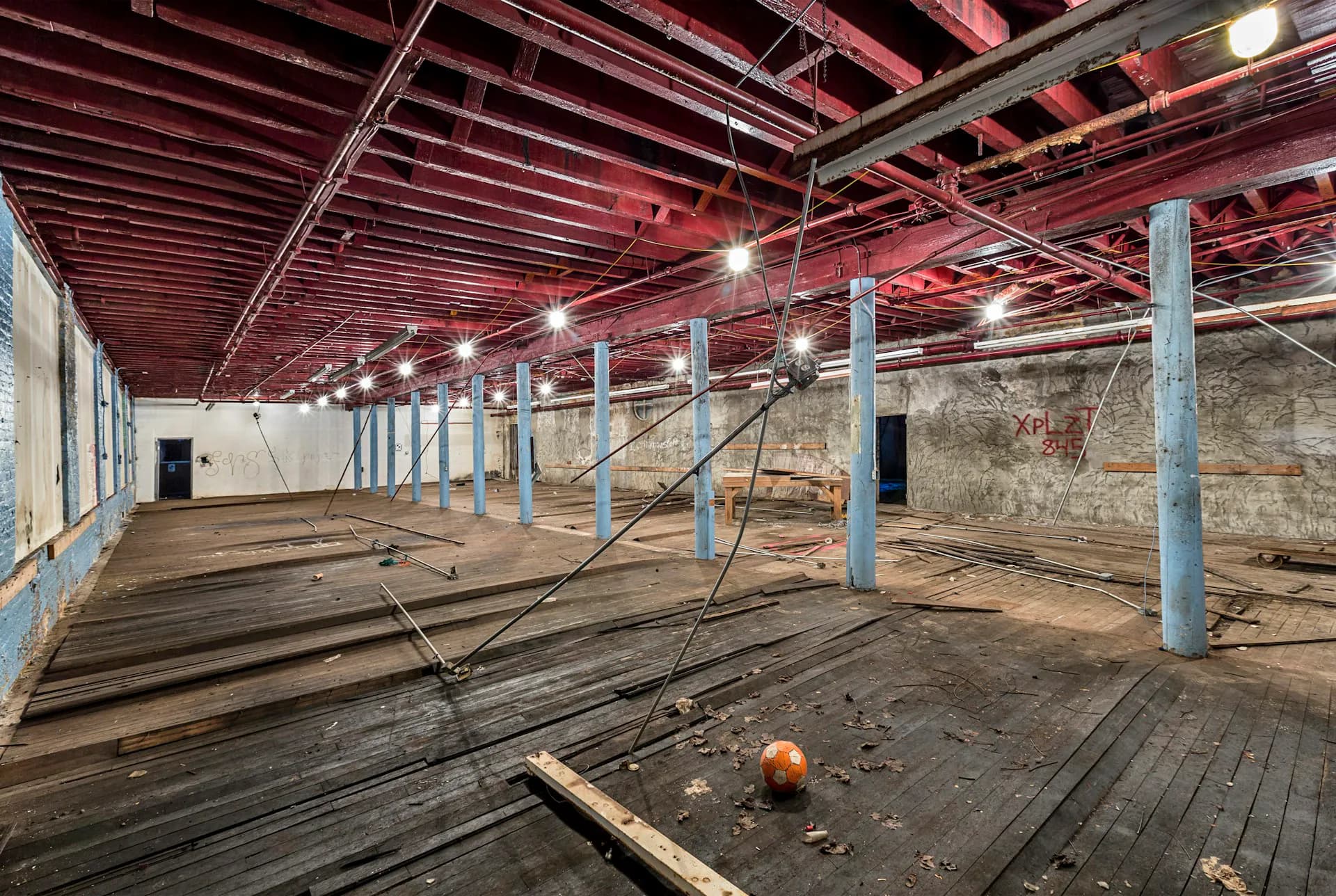 Industrial loft space with exposed red ceiling beams, blue support columns, wooden flooring, and large windows, designed by Henson Architecture.