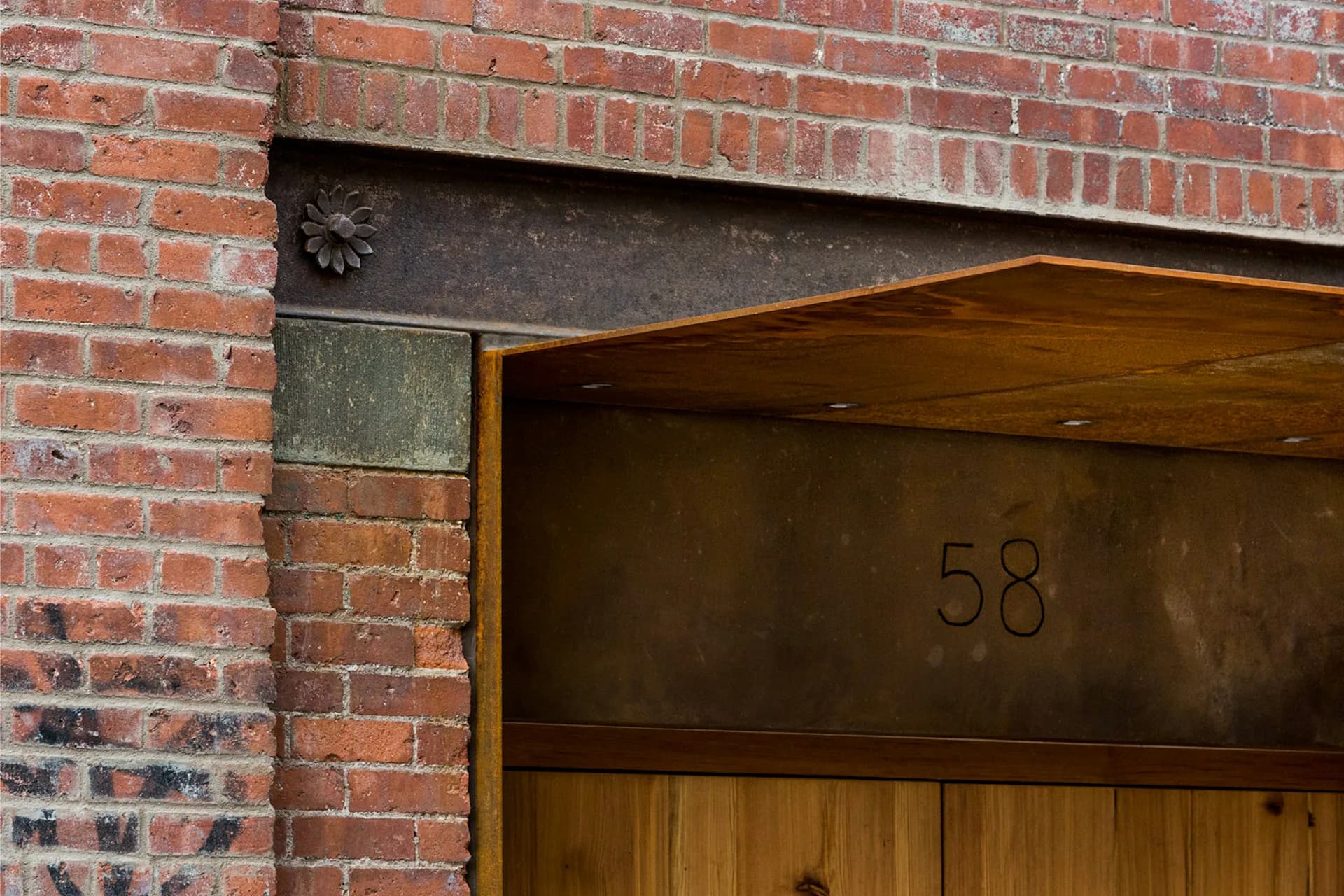 Modernist residential entrance featuring a bronze door with numerals 58, wood detailing, and red brick facade by Henson Architecture.