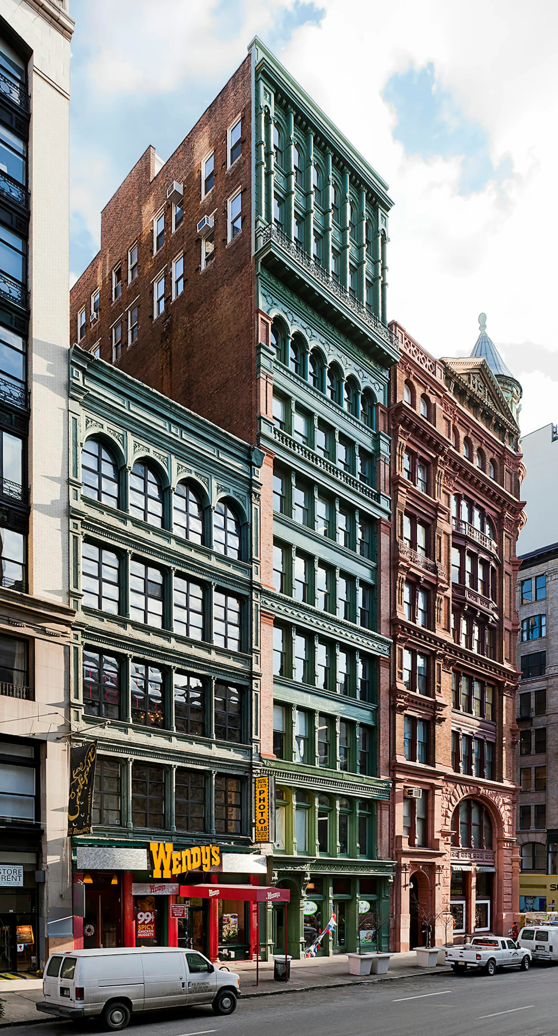 Historic facade restoration featuring brick and cast-iron storefronts with green and red painted details, street-level retail including Wendy's signage, by Henson Architecture.