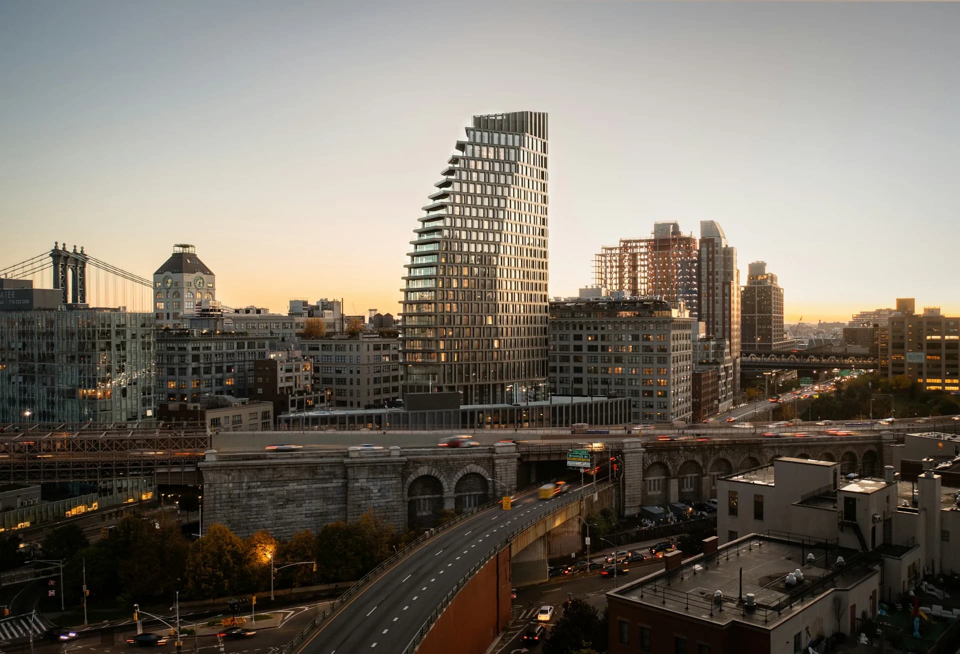 Sunset photograph of a mixed-use urban skyline featuring a distinctive diagonal-striped residential tower among historic buildings and street-level infrastructure by Hill West Architects.