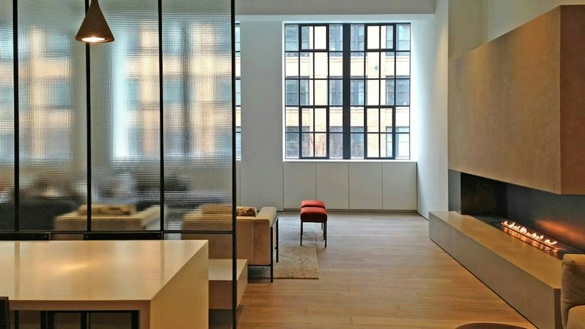 Modern loft interior with light wood flooring, glass partitions, linear fireplace, and large grid windows, designed by Hirsch Corti Architecture.