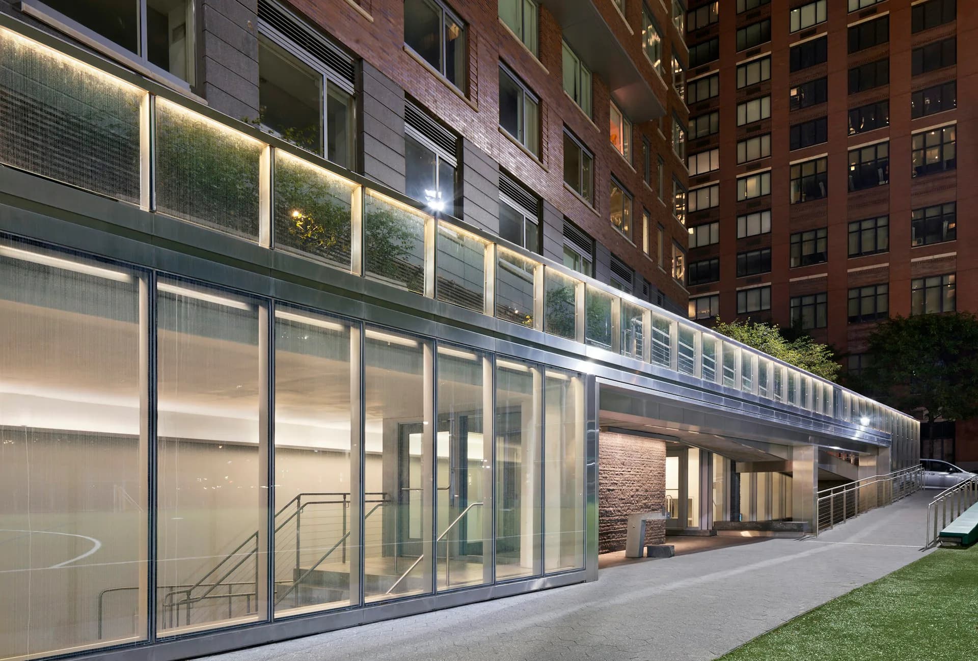 Modern ground-floor retail or gallery space with floor-to-ceiling glass facades, minimal interior furnishings, warm lighting, and adjacent green lawn by HMA | Hanrahan Meyers Architects.