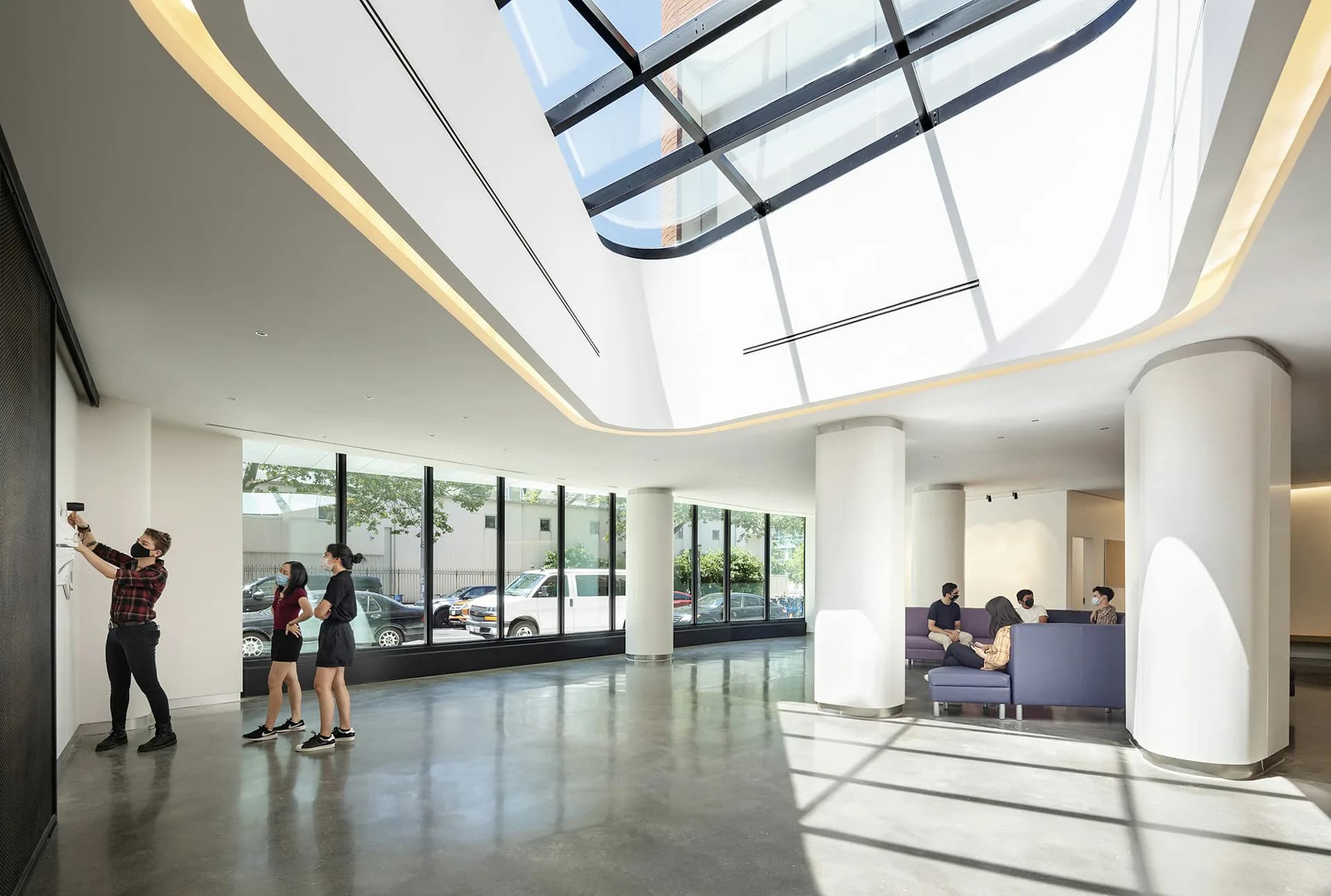 Bright modern lobby with skylights, polished concrete floors, cylindrical white column, and groups of people; designed by HMA | Hanrahan Meyers Architects.
