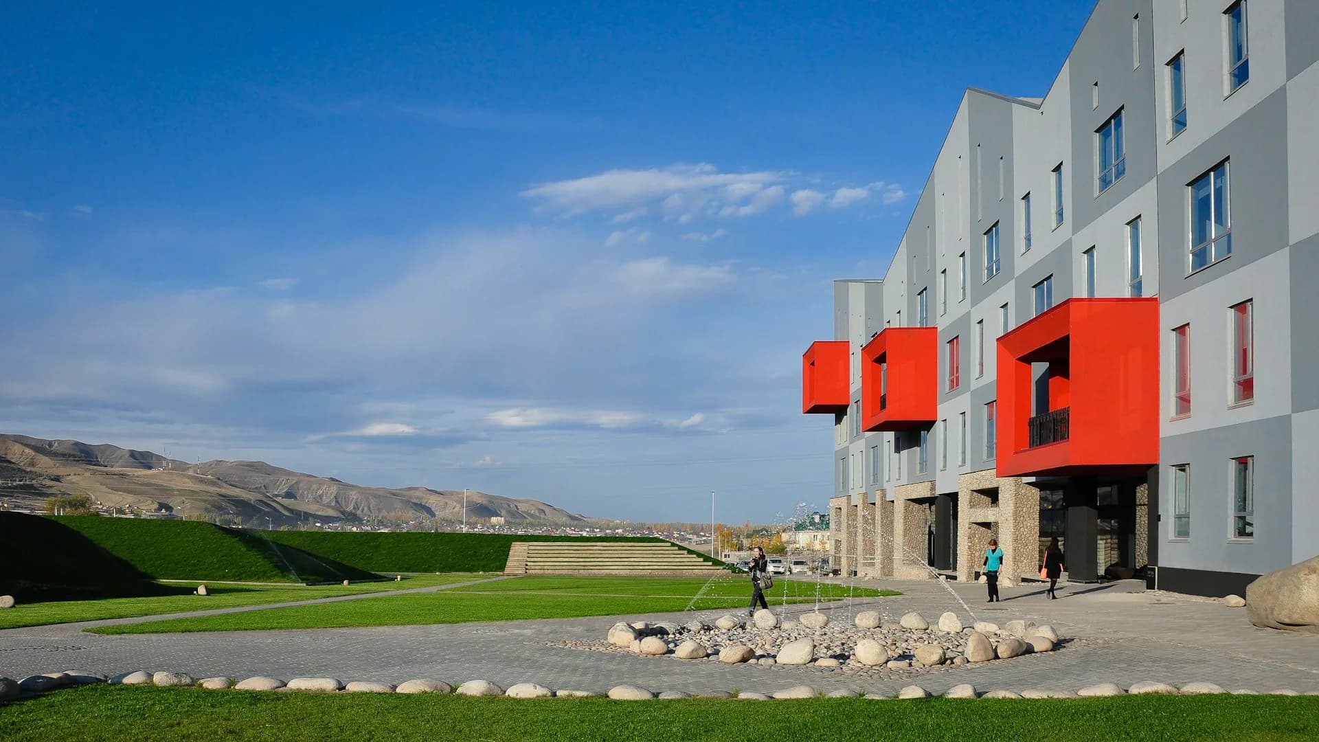 Modern residential building with distinctive red modular balconies set in a landscaped courtyard with green lawn and mountain views, by HMA2 Architects.
