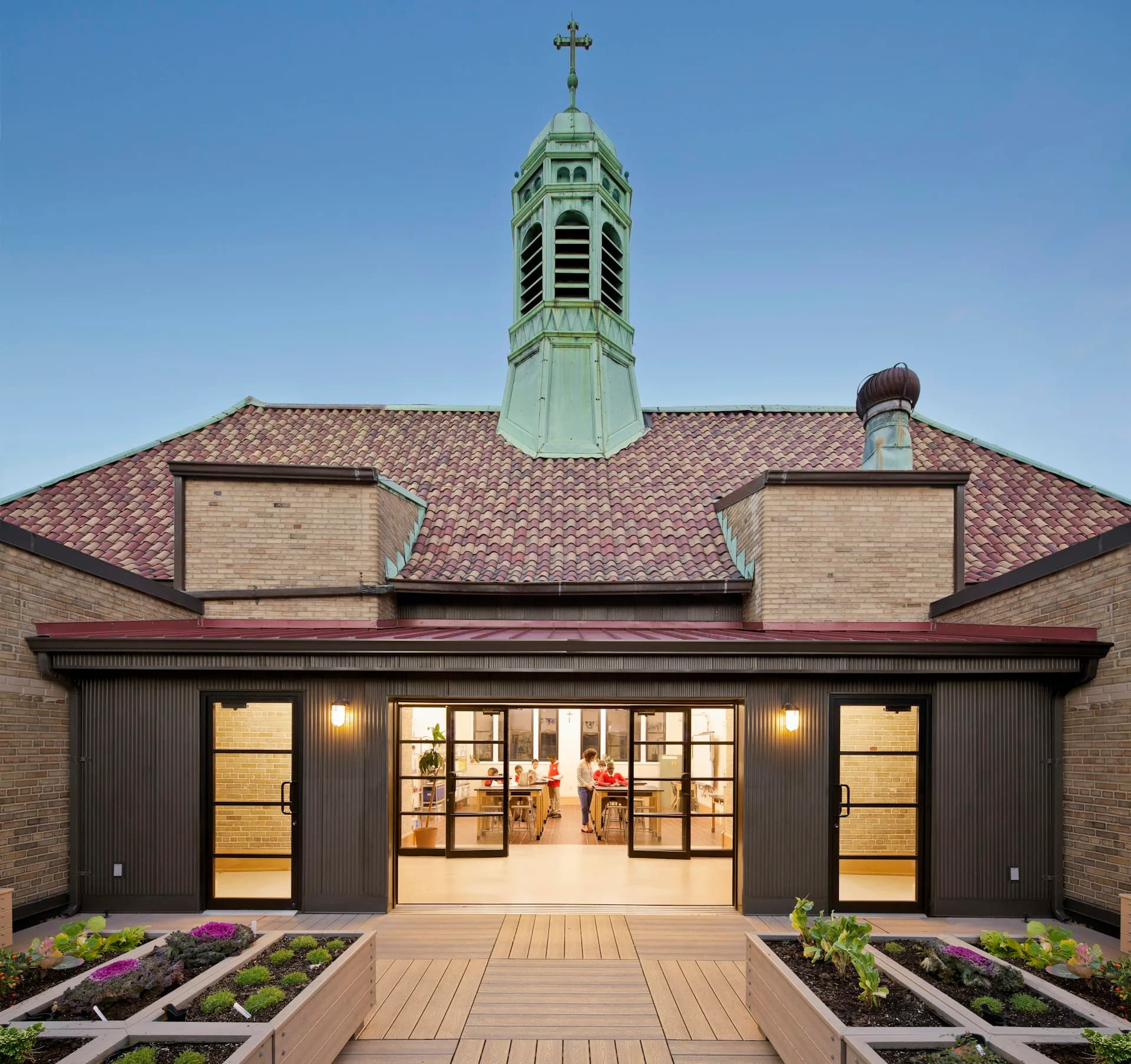 Modern brick addition with black-framed glass doors opens to wooden deck, featuring a historic church tower backdrop, designed by HMA2 Architects.