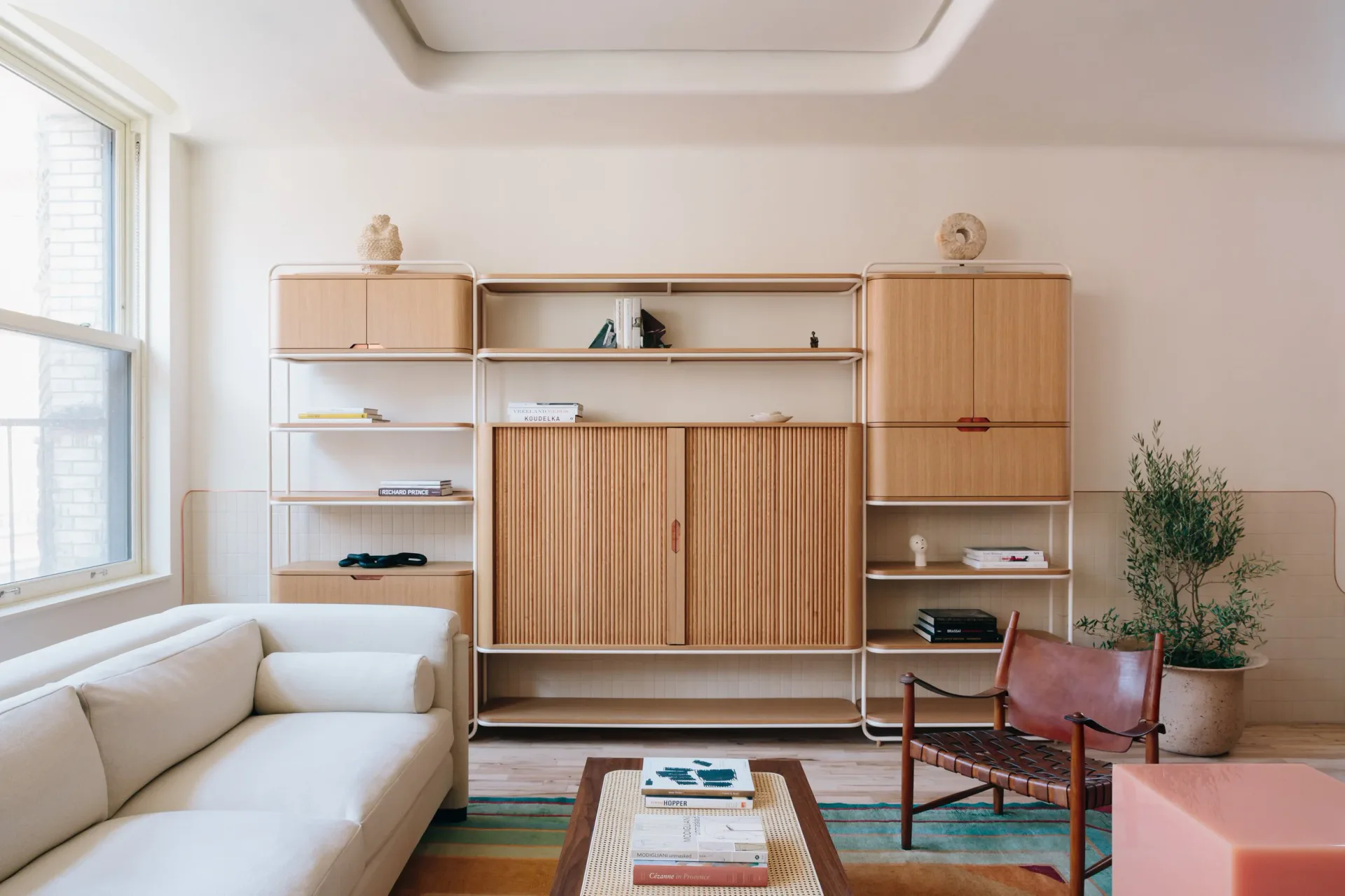 Minimalist living room with natural wood cabinetry, cream sofa, colorful geometric rug, and vintage furniture by Home Studios.