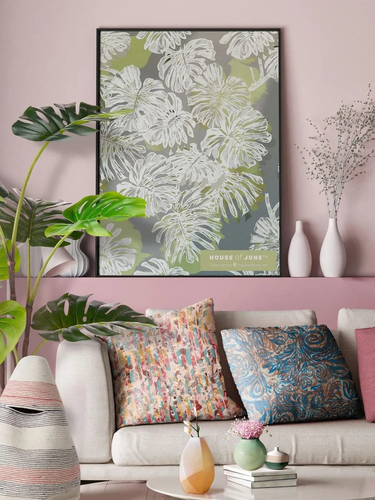 Living room with pink wall, cream sofa, patterned pillows, potted plants, and botanical artwork above by House of June.