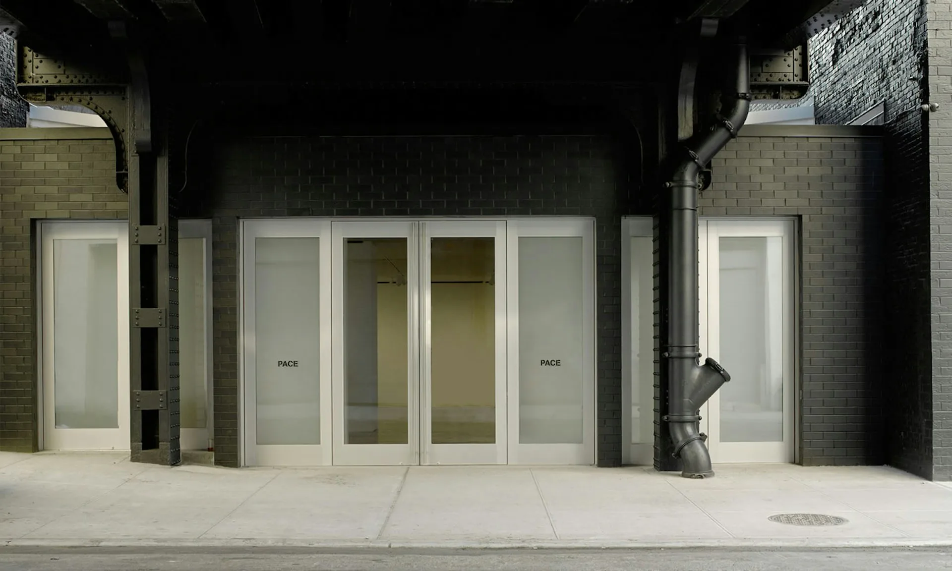Minimalist storefront with white glass doors and panels set against dark tile walls, featuring clean geometric lines and a monochromatic palette by HS2 Architecture.