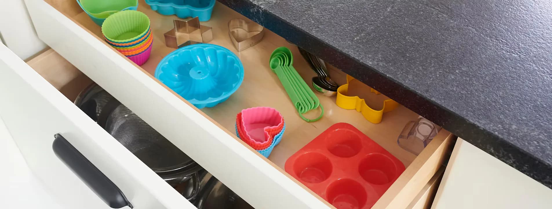 Open drawer with custom wooden organizer insert featuring colorful silicone molds and kitchen tools, showcasing refined storage design by Hub Woodworks.