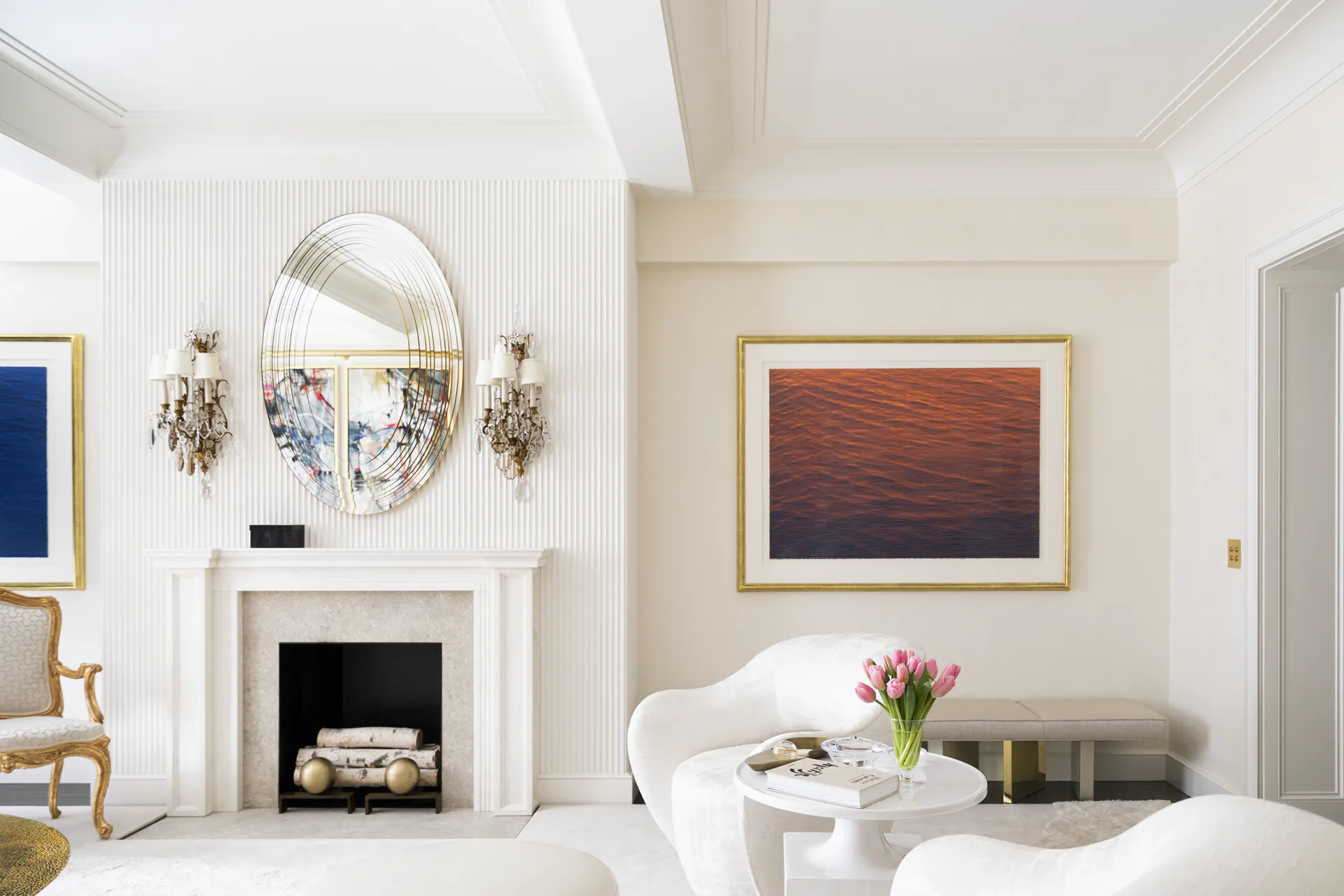 Elegant living room with white paneled fireplace, gold-framed mirror, decorative sconces, and refined furnishings in cream and gold tones by Hyde Park Mouldings.