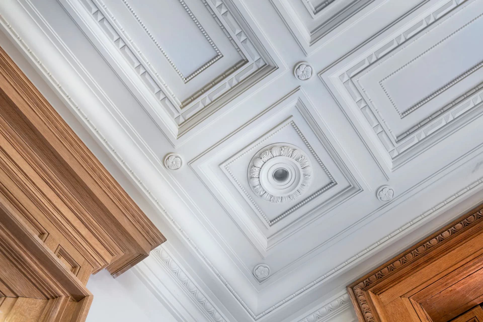 Ornate white ceiling with coffered panels, decorative rosette medallion, and wooden door frame detailing by Hyde Park Mouldings.