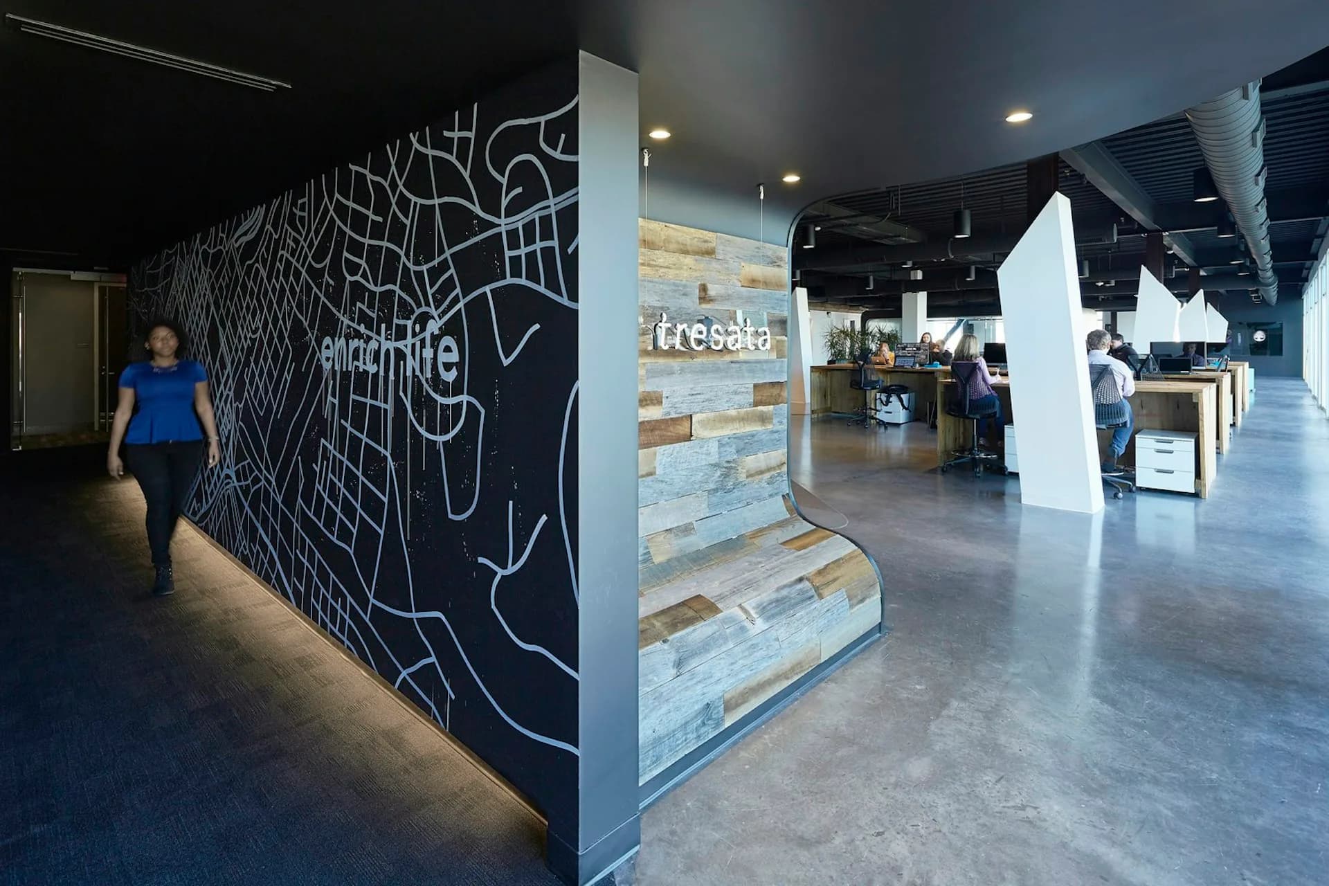 Modern interior space with black feature wall displaying white geometric line artwork, concrete flooring, and contemporary retail kiosk by IA.