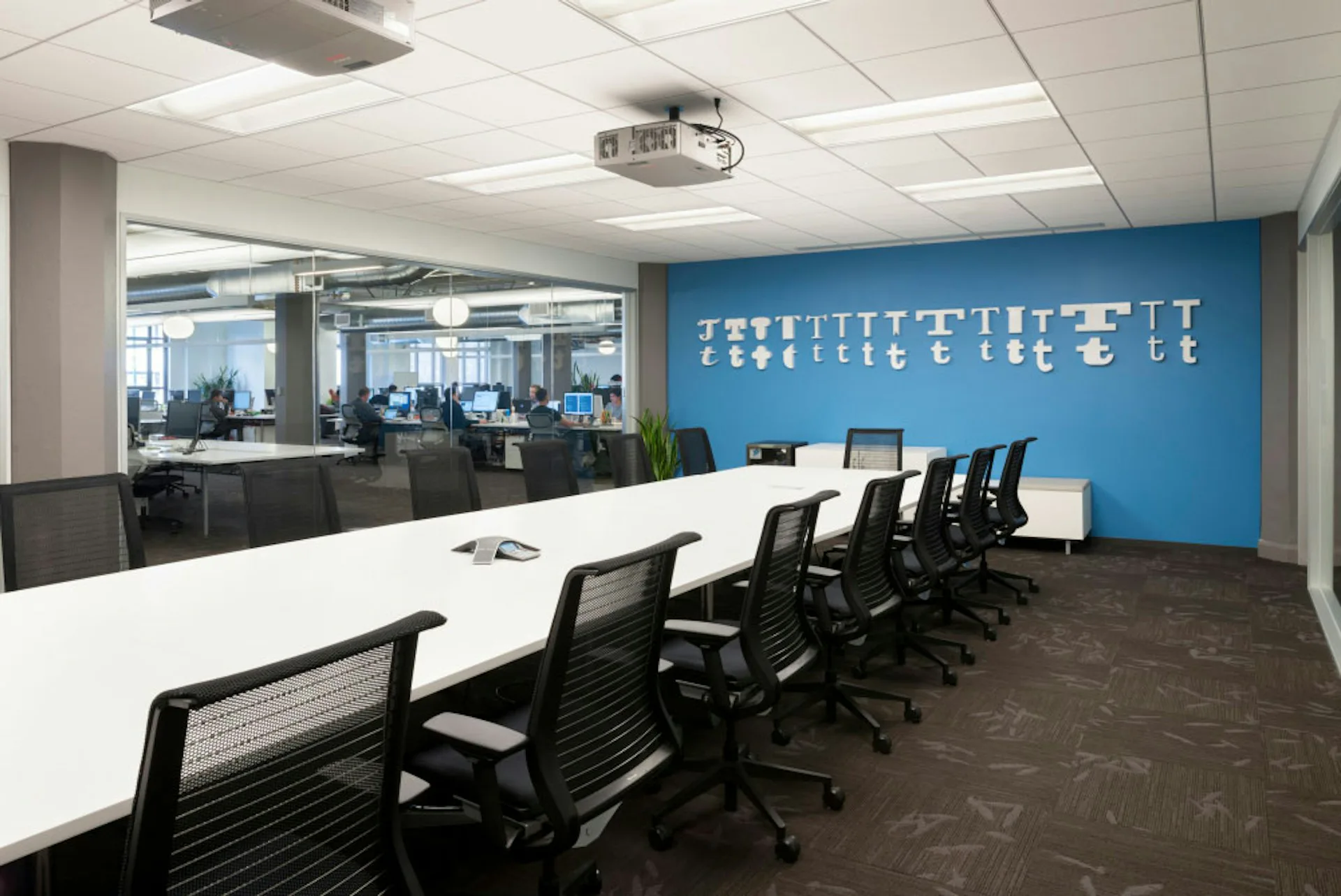 Modern conference room with white table, black ergonomic chairs, and striking blue accent wall featuring white silhouette graphics by IA.
