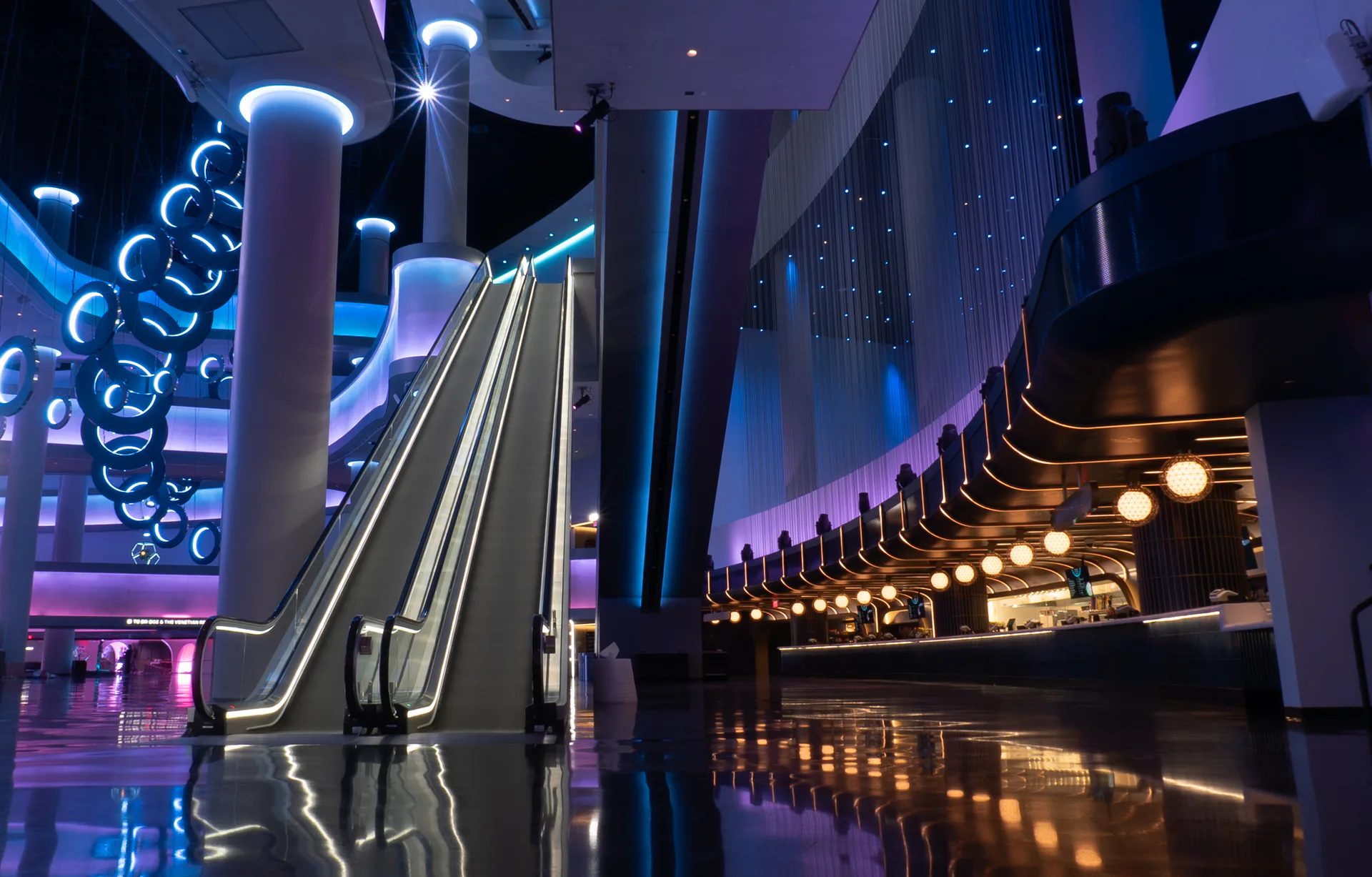 Futuristic nightclub interior with neon blue and purple lighting, escalators, mirrored surfaces, and glowing architectural elements by ICRAVE.