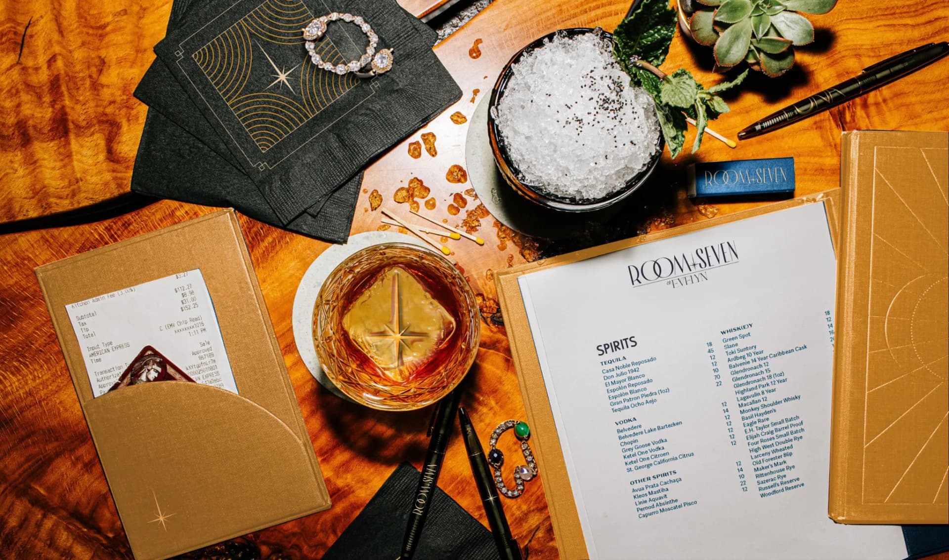 Overhead view of a styled bar or restaurant table setting featuring cocktails, menus, decorative objects, and warm orange and black tones by ICRAVE.