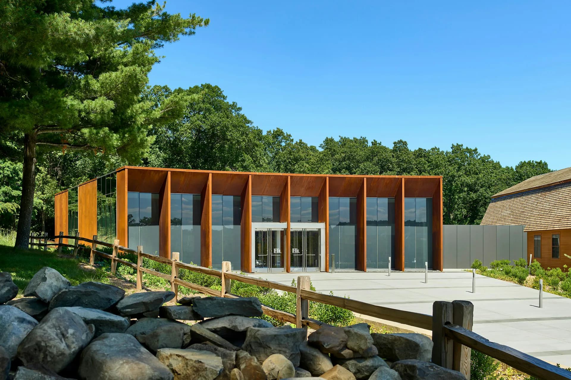 Modern residential pavilion with warm timber cladding and extensive glazing, elevated on concrete deck overlooking landscaped grounds with large boulders, by ikon.5 architects