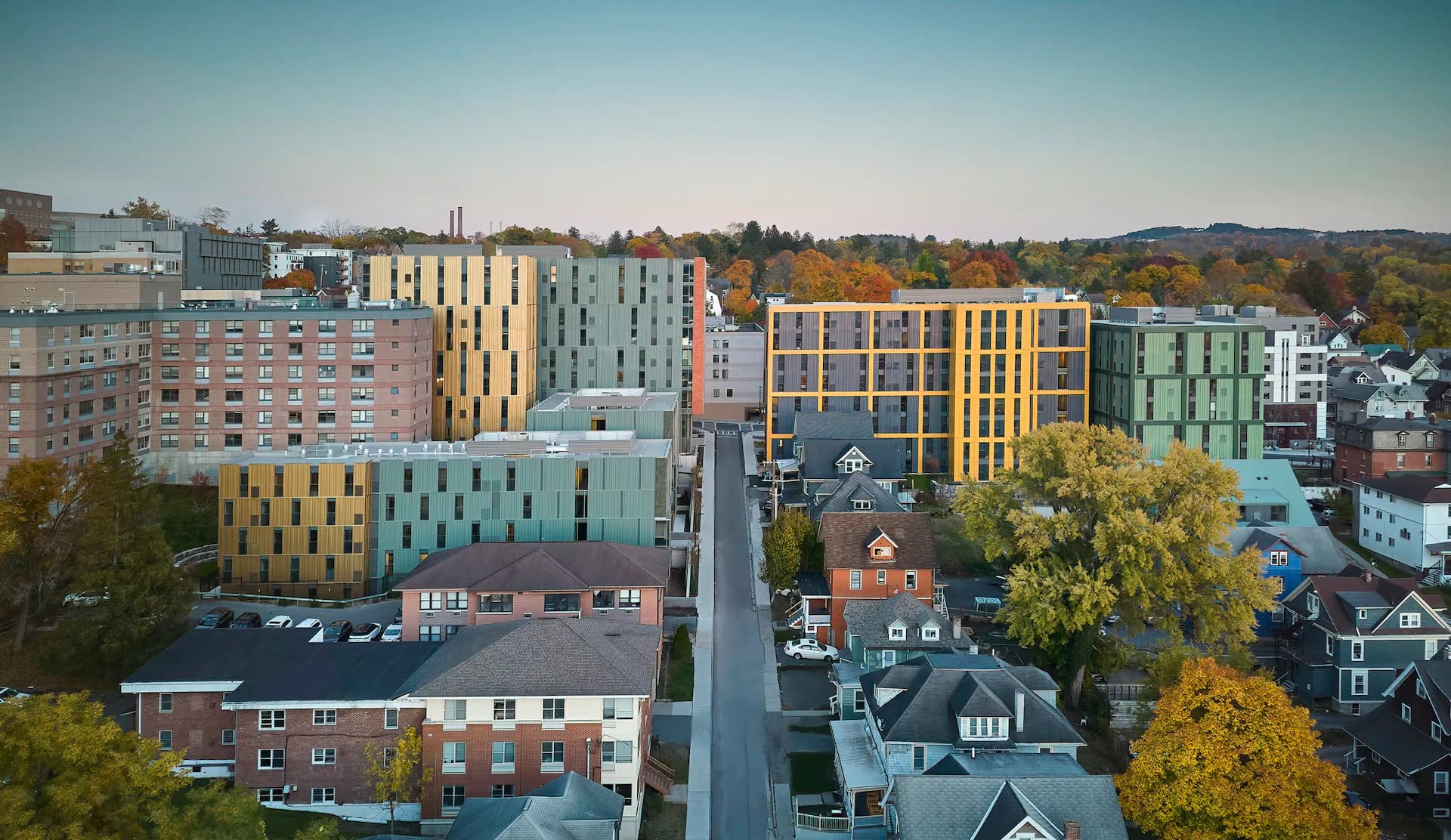 Urban residential neighborhood with modern colorful apartment buildings in autumn, featuring mixed-use architecture and tree-lined streets by ikon.5 architects.