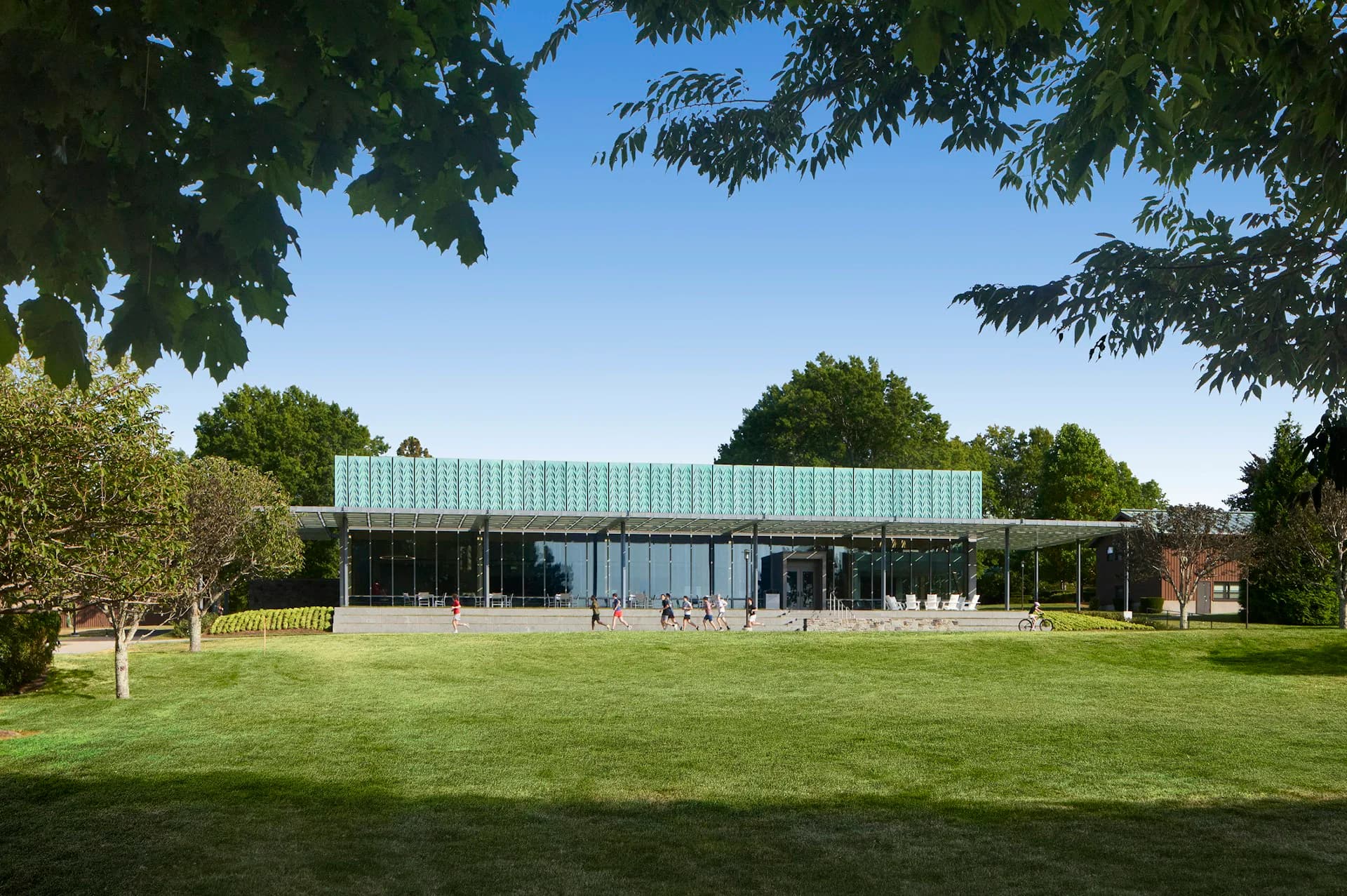 Modern glass and turquoise metal-clad pavilion with open lawn and mature trees, designed by ikon.5 architects.
