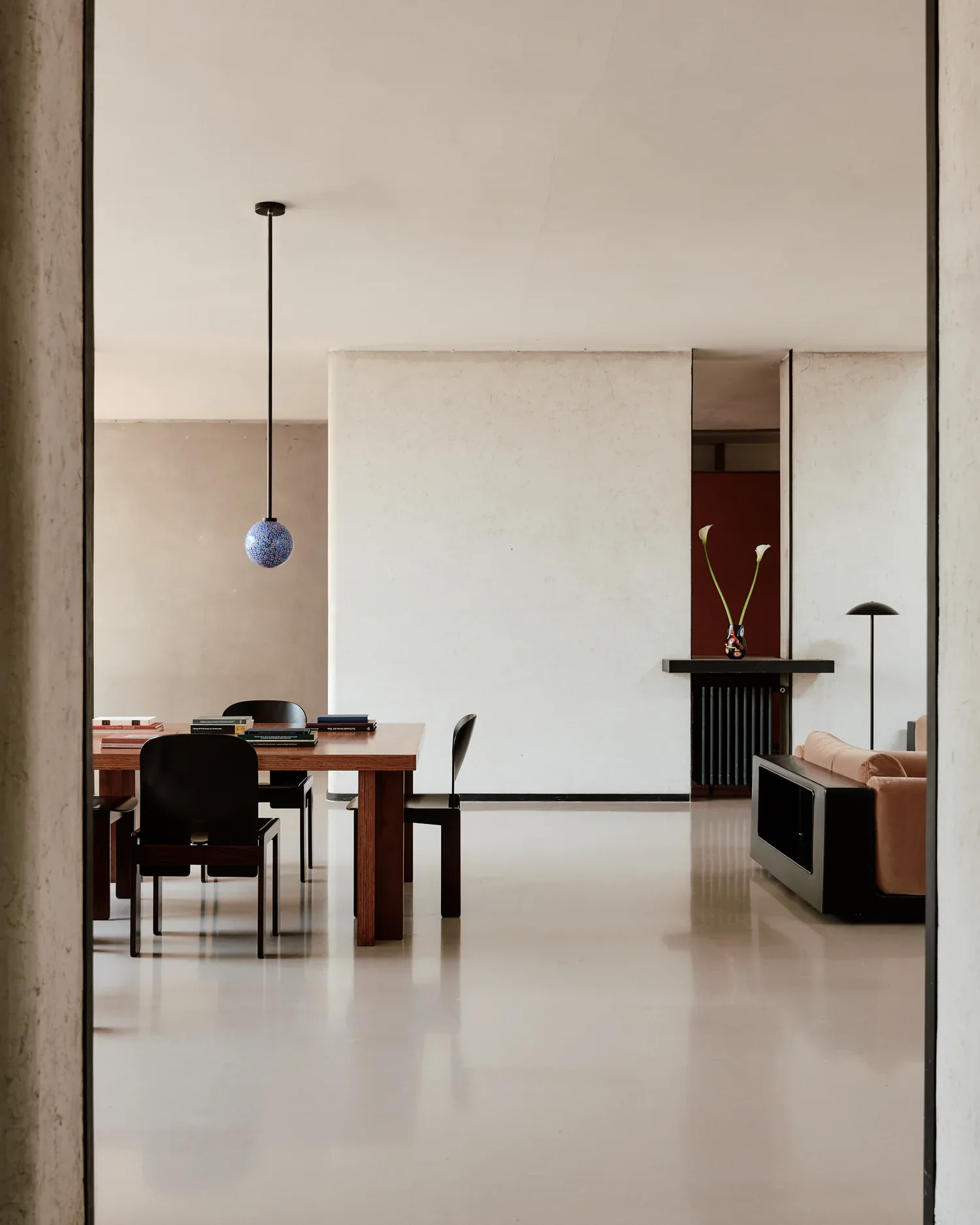 Minimalist interior space with polished concrete floors, wooden furniture, and a blue pendant light, designed by In Common With.