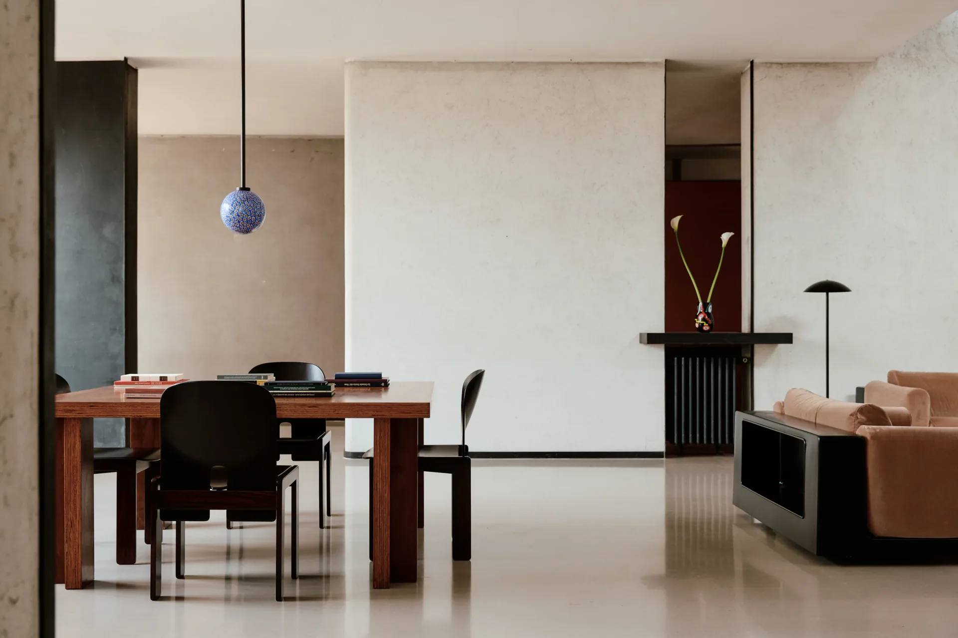 Minimalist office interior with warm wood desk, black chairs, large white panel divider, and muted earth tones by In Common With.