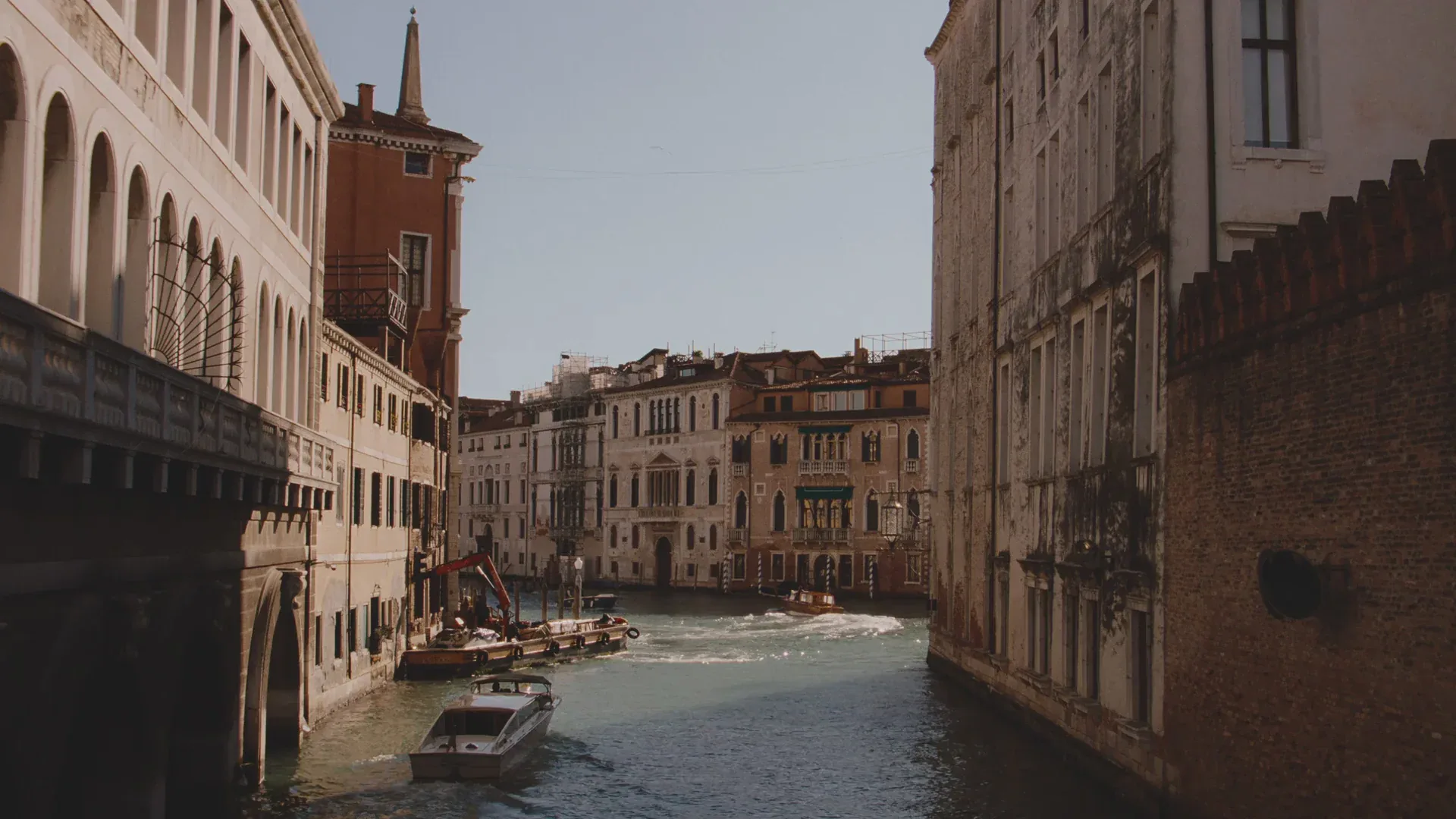 Grand Canal waterfront in Venice with historic terracotta and cream-colored buildings reflected in calm water by In Common With.
