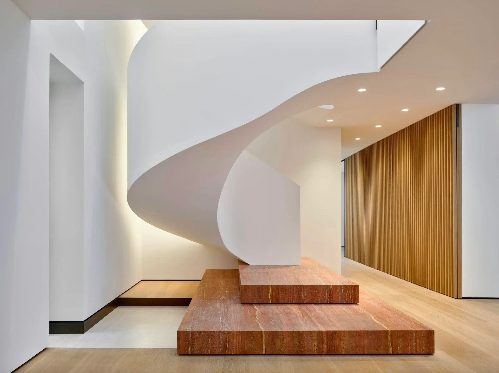 Minimalist interior with curved white walls, wooden stepped platform, warm lighting, and vertical wood slats by IN STUDIO.