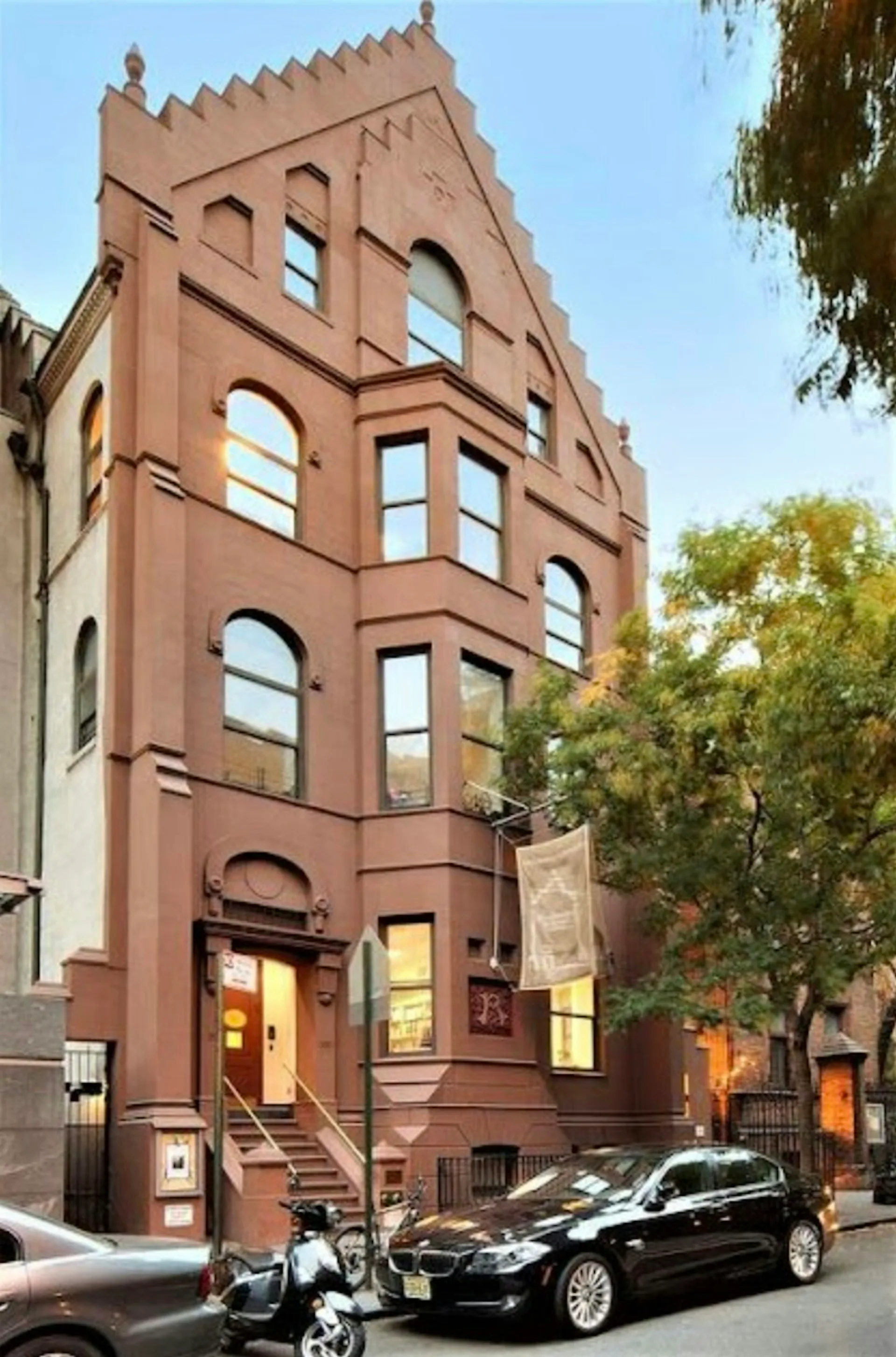 Renovated historic brick townhouse facade with arched windows, crenellated roofline, and ground-level retail entrance by IN STUDIO.