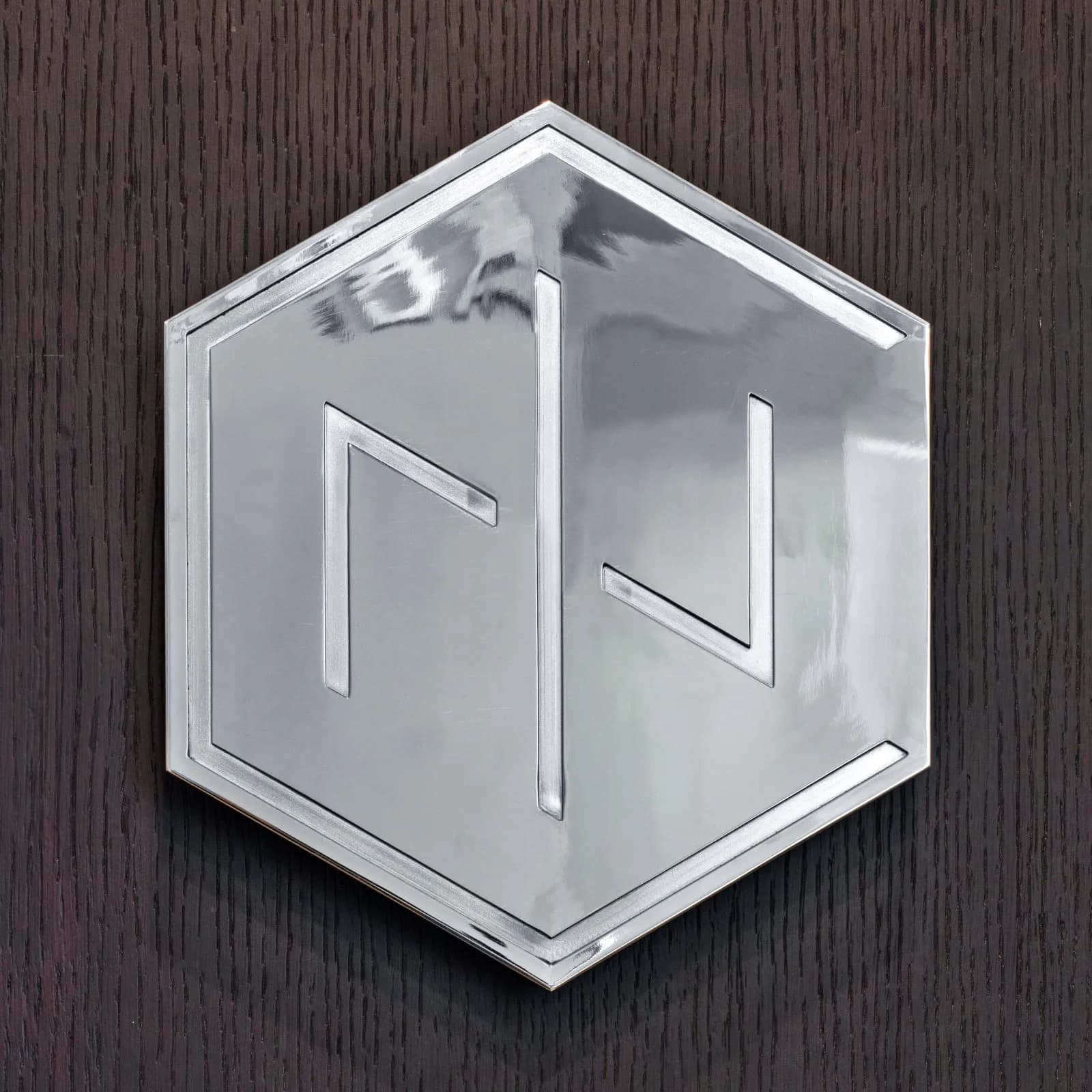 Geometric hexagonal mirror with metallic frame mounted on textured dark wood wall, featuring clean lines and minimalist design by INC Architecture & Design.