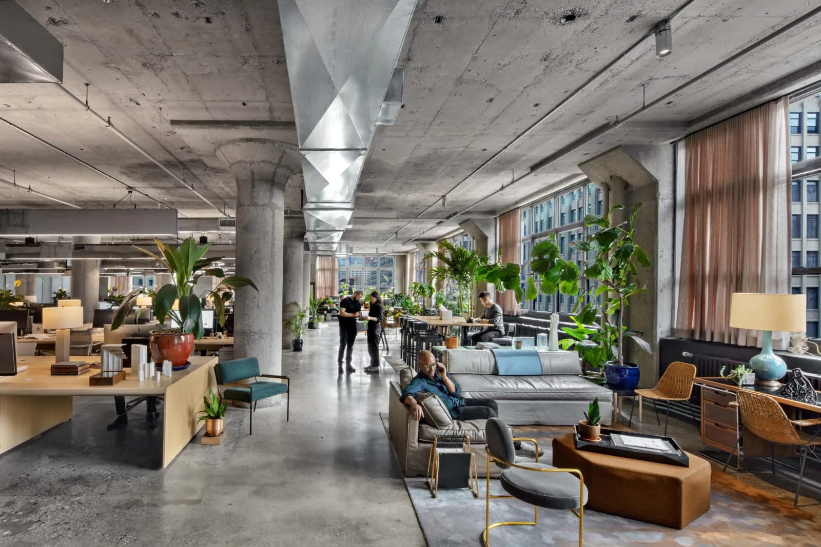 Modern open-plan office with exposed concrete ceiling, wooden furniture, lush greenery, and natural light, designed by INC Architecture & Design.