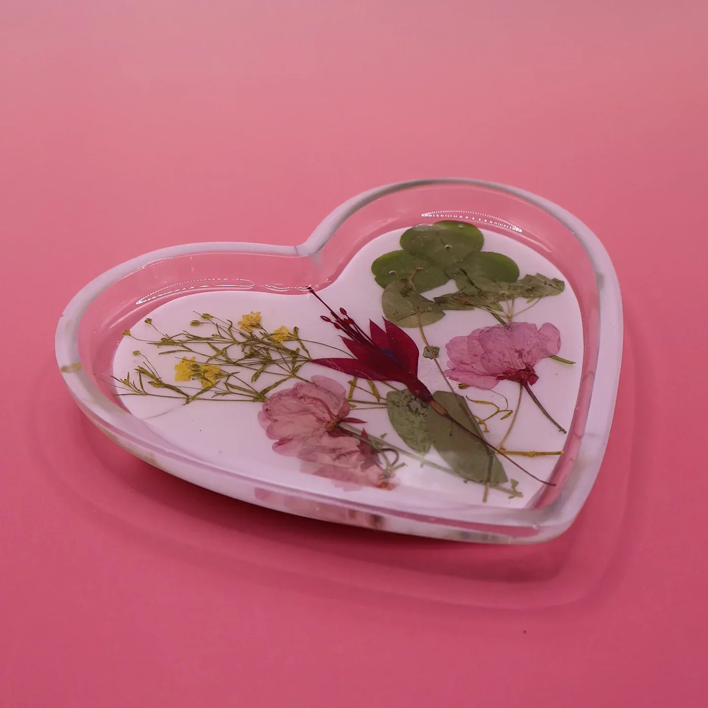 Heart-shaped resin keepsake with pressed flowers and botanical specimens preserved under clear acrylic by IRUSU Creation.