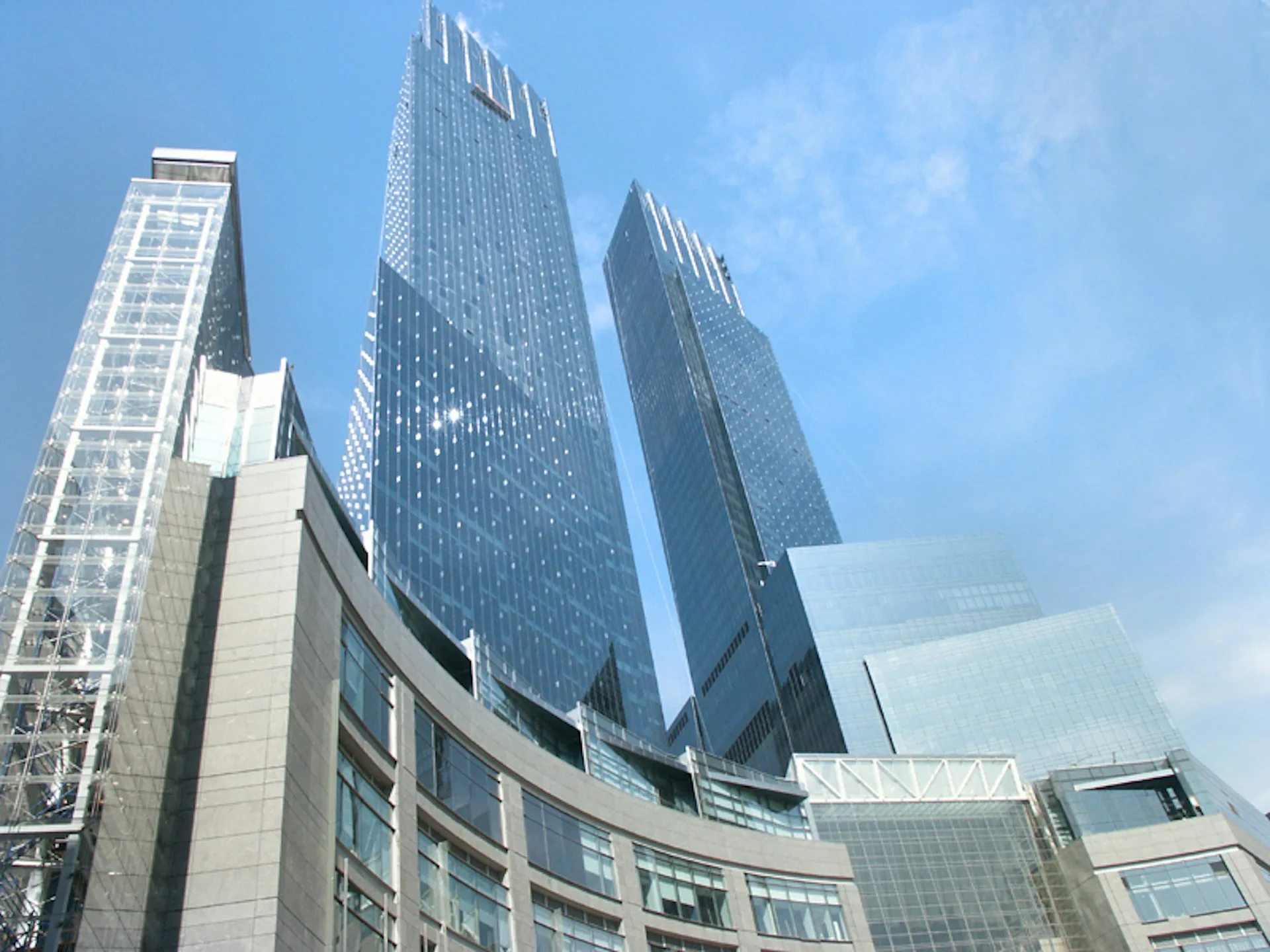 Modern glass and steel high-rise towers with curved facades and reflective surfaces rise against a blue sky, showcasing contemporary urban architecture by Ismael Leyva Architects, P.C.