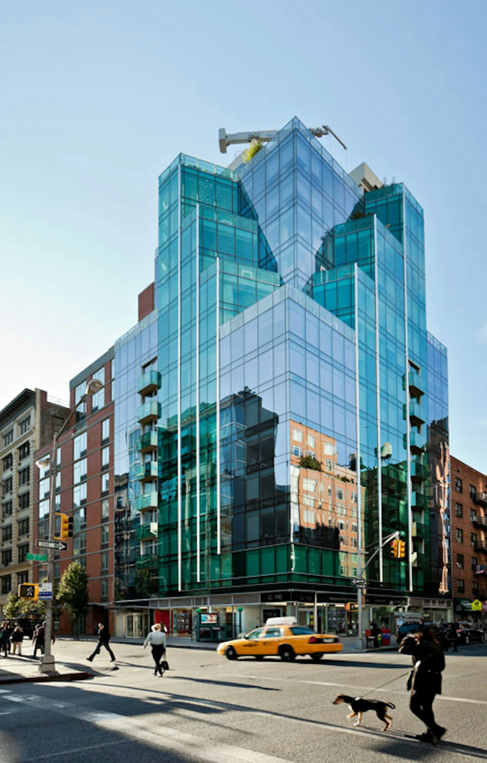 Modern glass and turquoise-paneled mixed-use tower with geometric facade, street-level retail, and adjacent historic brick buildings in urban setting by Ismael Leyva Architects, P.C.